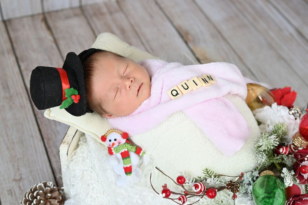 Sleeping baby in Christmas outfit with snowman decorations and festive accessories.