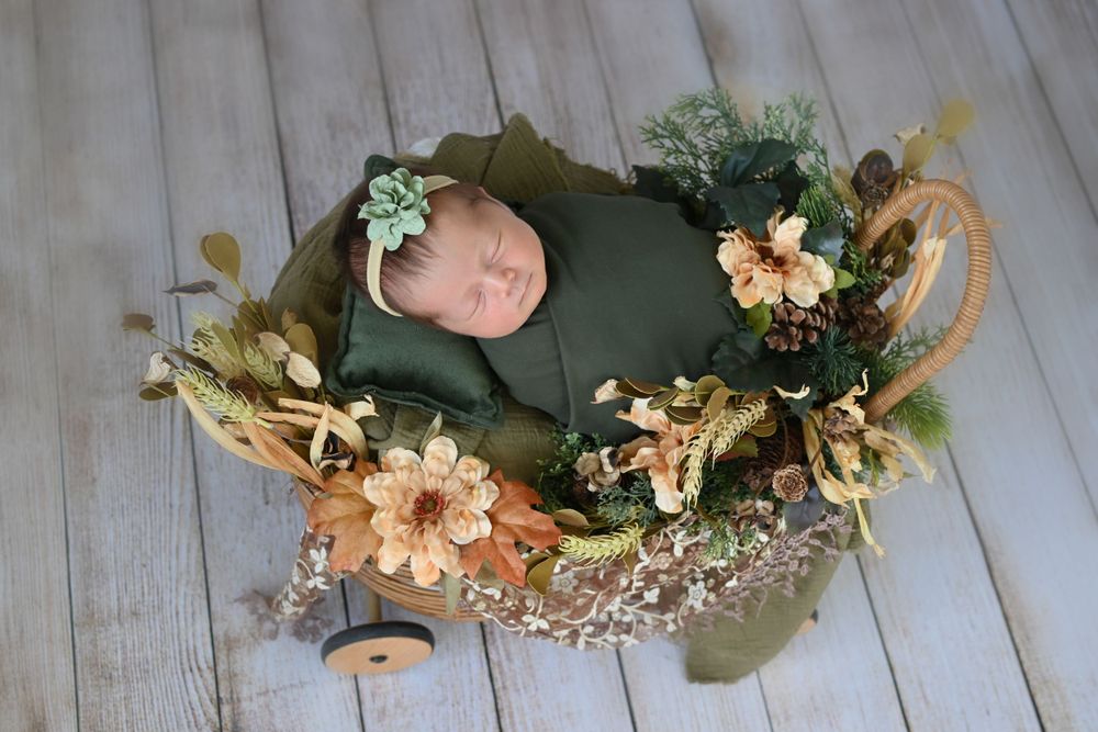 Newborn baby sleeping in green wrap surrounded by autumn floral decorations.