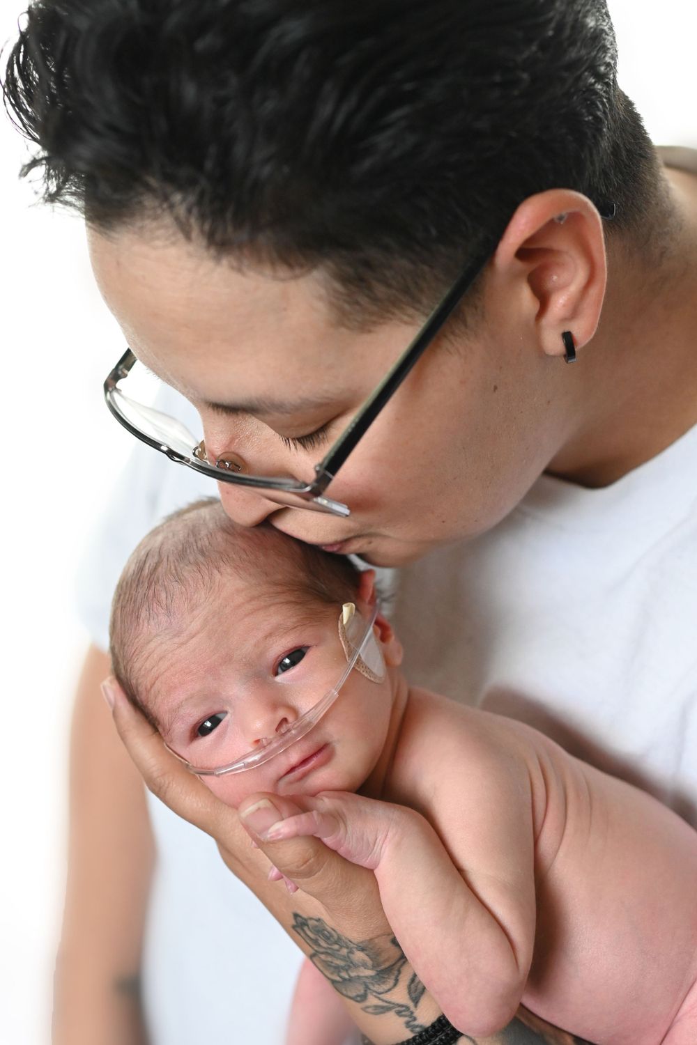 Close-up portrait with newborn baby showing medical tubes against white background.