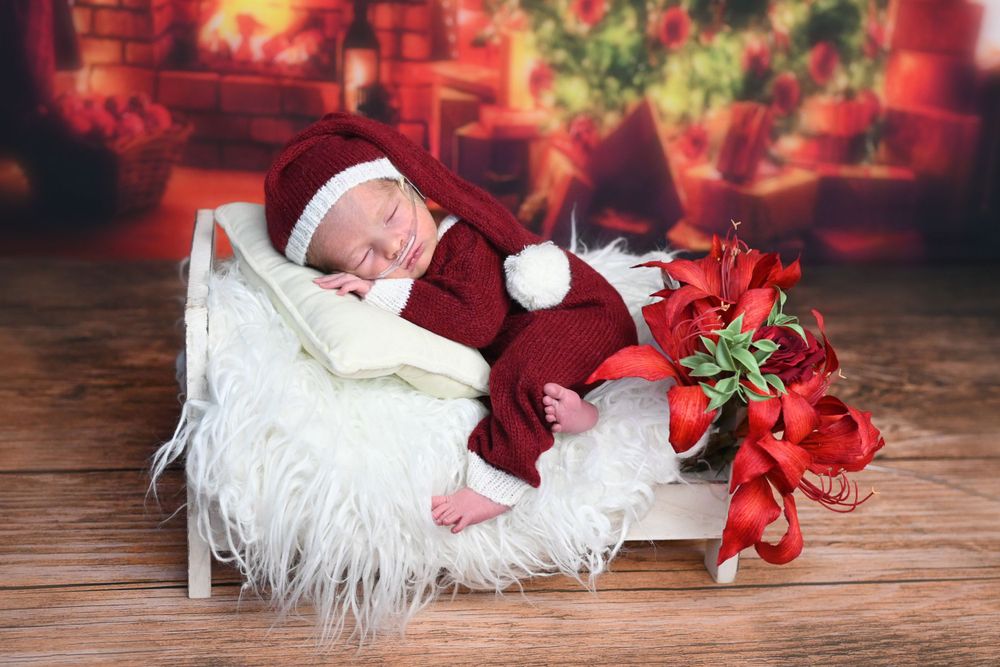 Sleeping baby in Santa outfit on white fur with Christmas decorations.