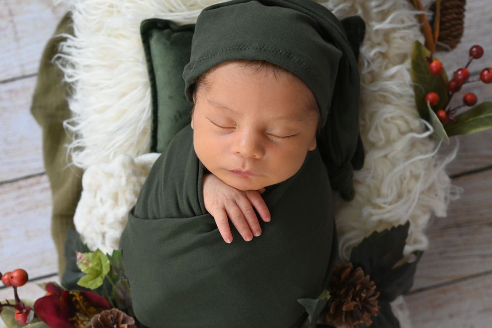Sleeping newborn in dark green wrap and hat with holiday decorations.