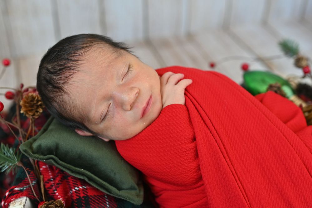 Holiday newborn photography with baby in red outfit against woodgrain background.