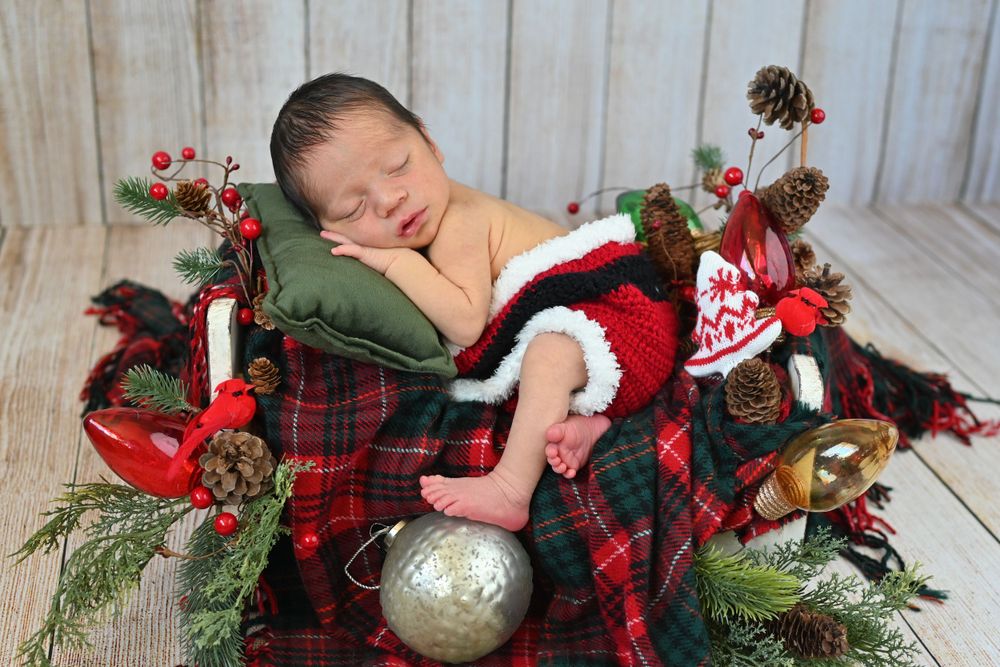 Holiday themed newborn photo with ornaments and plaid fabric decorations.