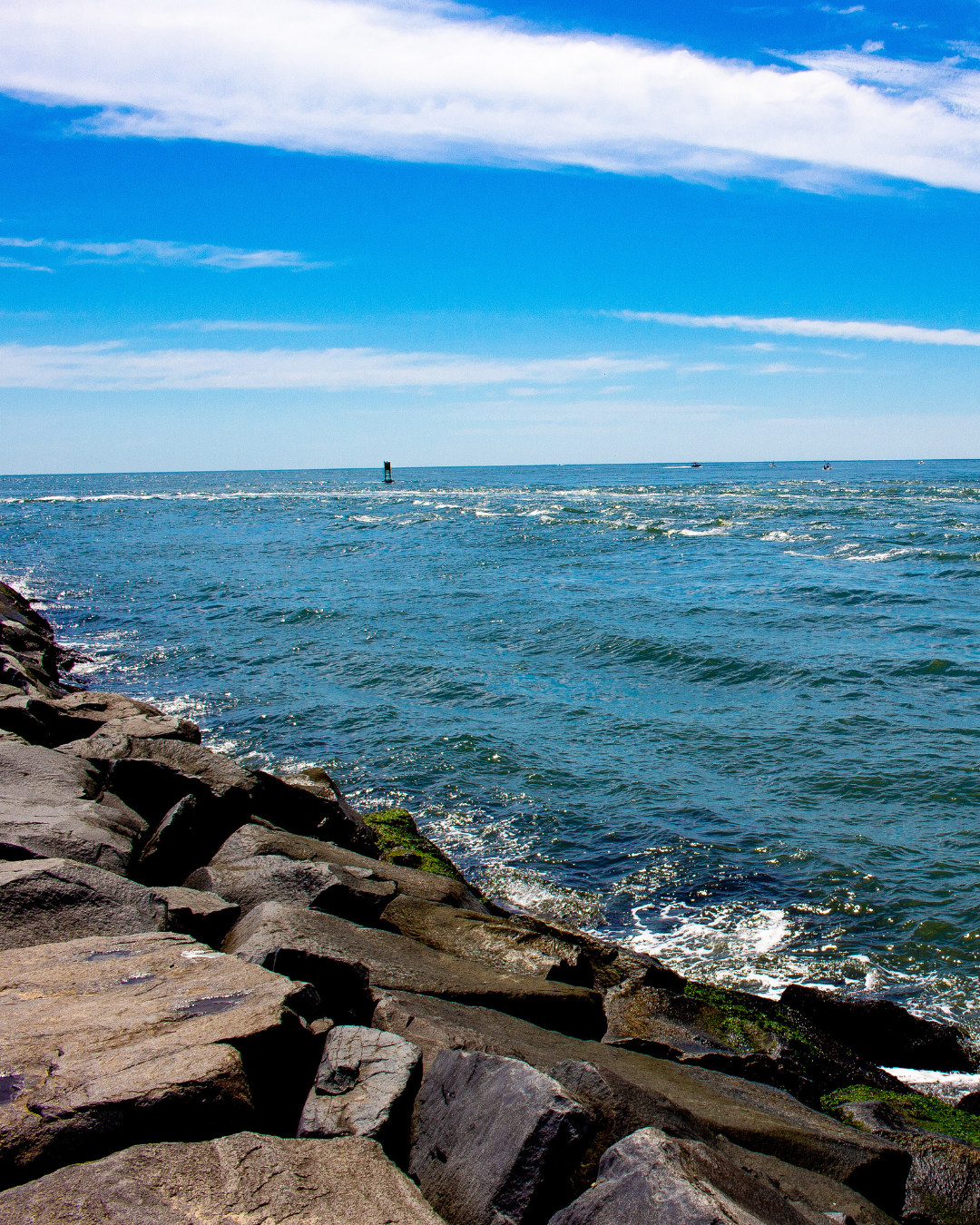 Rocky coastline with waves crashing against shore under bright blue sky.  L Visions Photography. Delaware.