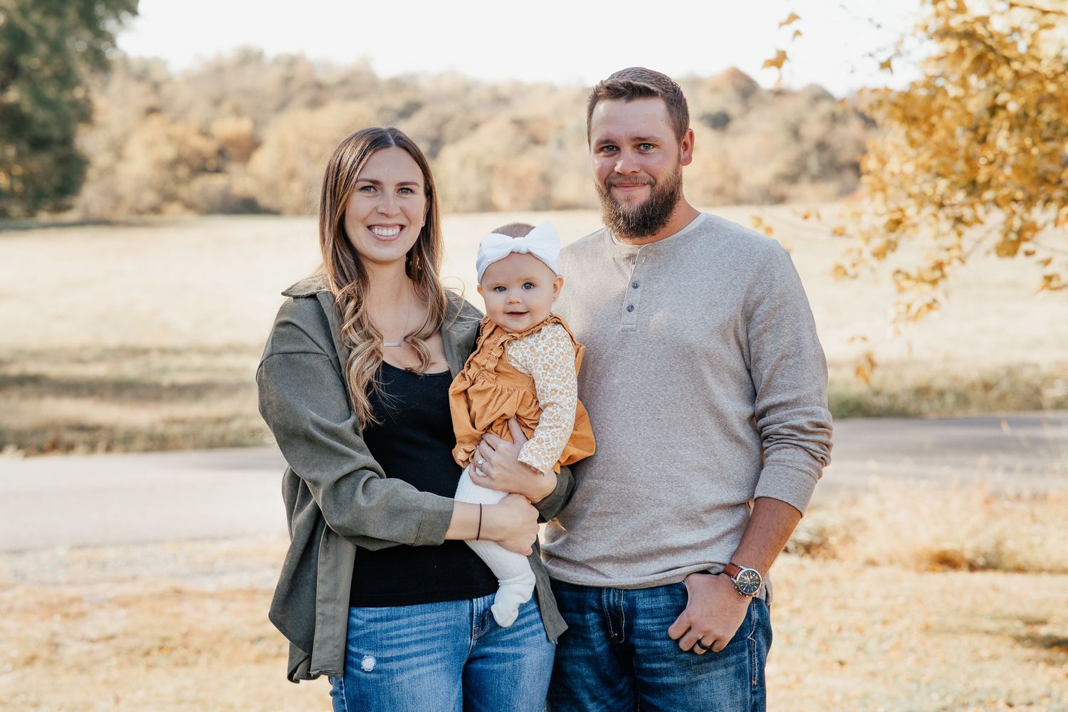 Casual outdoor family portrait in autumn with golden sunlight filtering through trees.