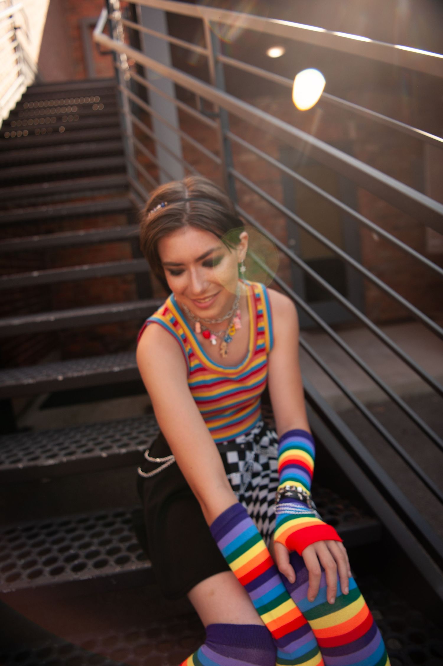 Someone wearing colorful rainbow striped arm warmers sits on metal stairs in dynamic lighting.