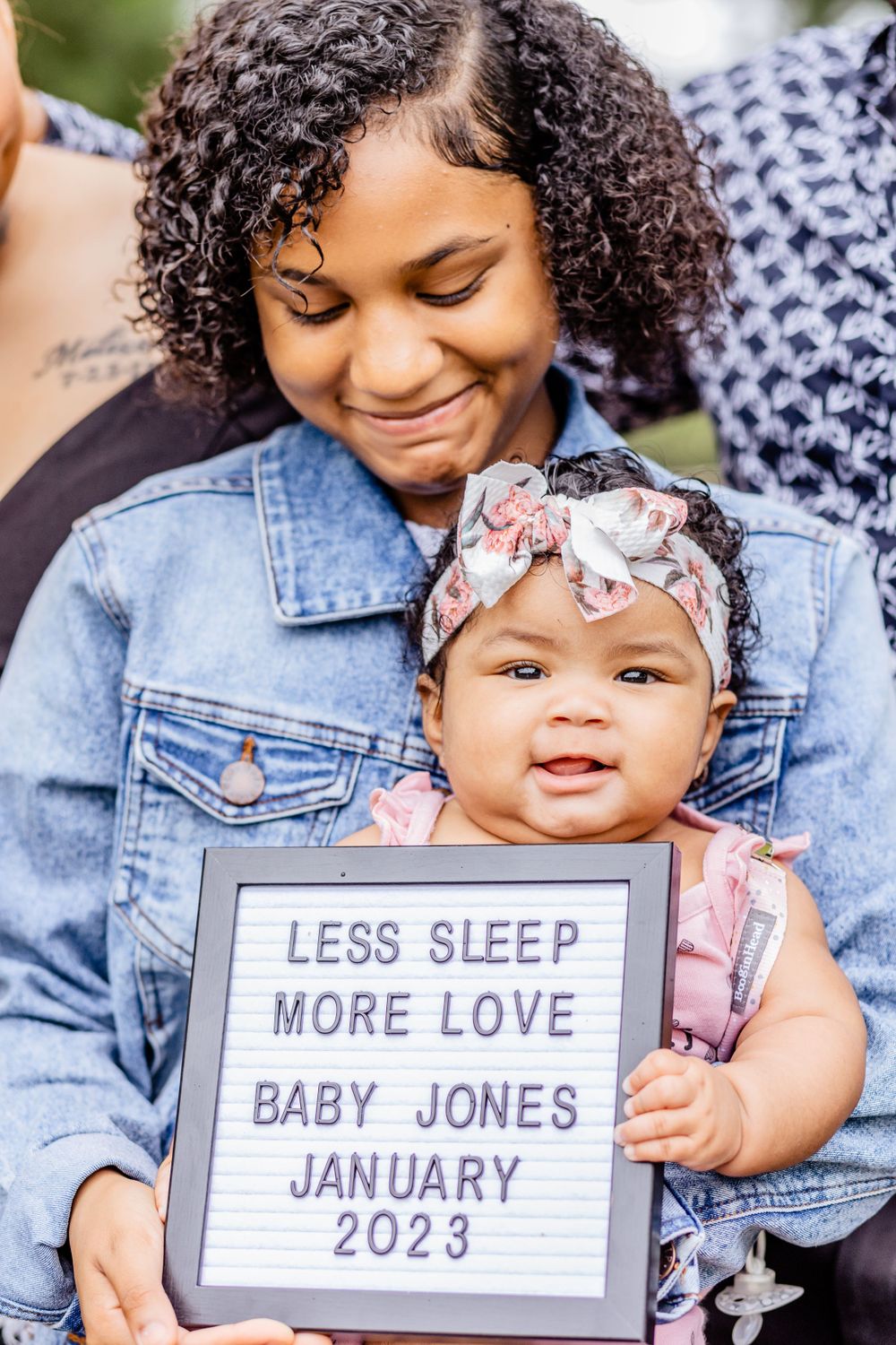 A baby announcement photo featuring a letterboard with baby details and floral headband.