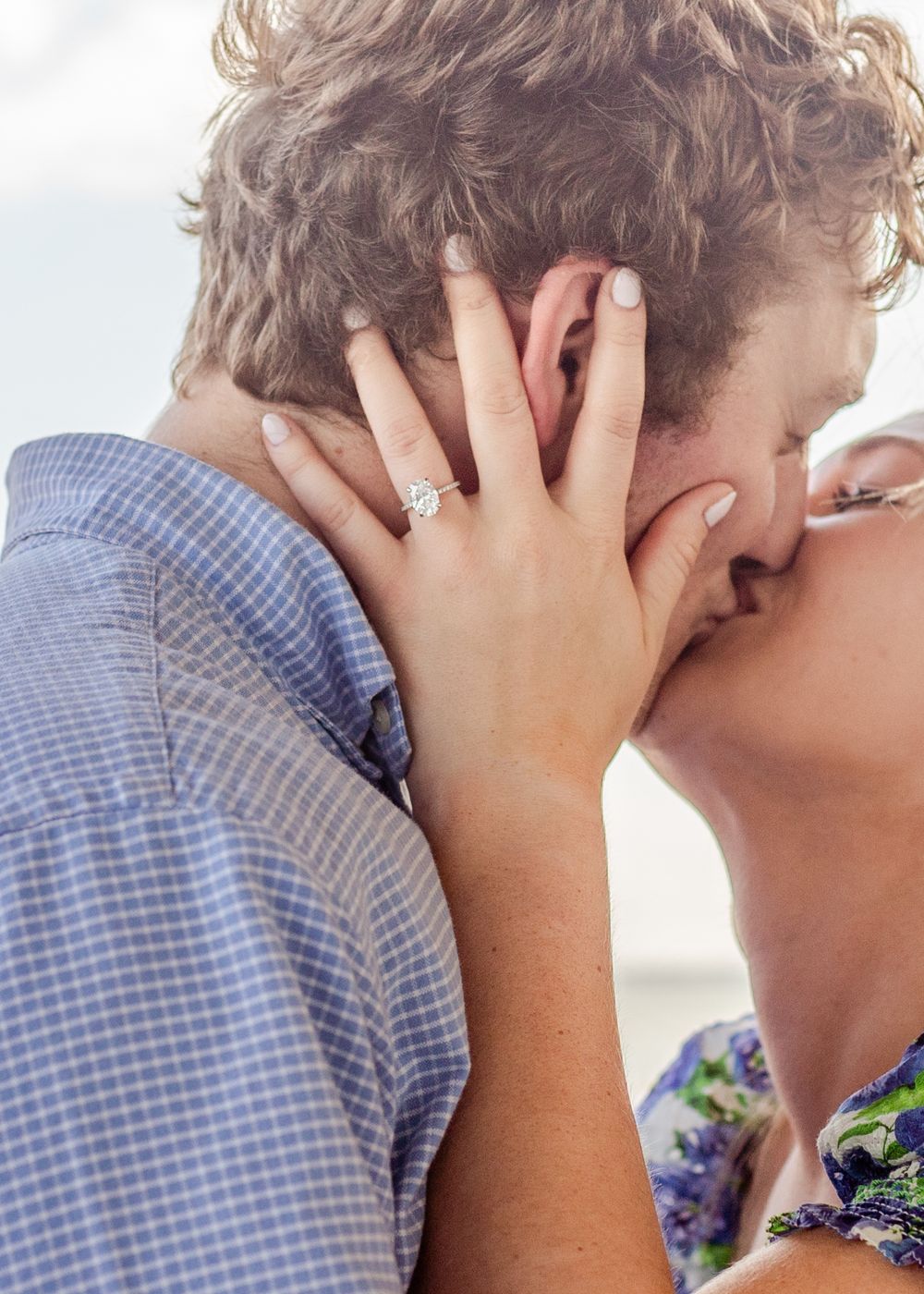 Close-up of a romantic kiss with a sparkling engagement ring visible on the hand.