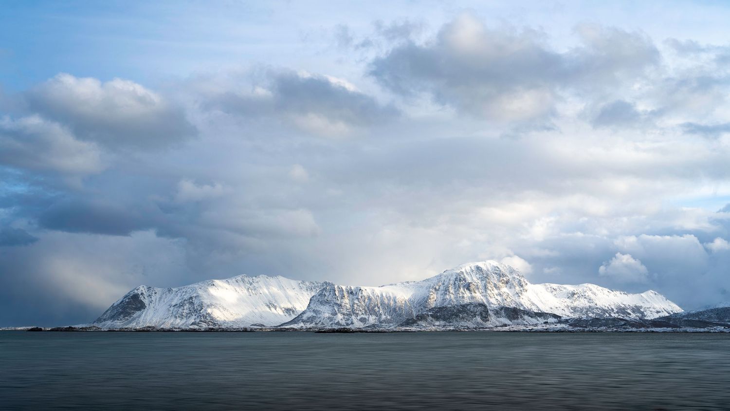 Rugged snow-covered mountains stretch across the horizon with dramatic cloud formations above.