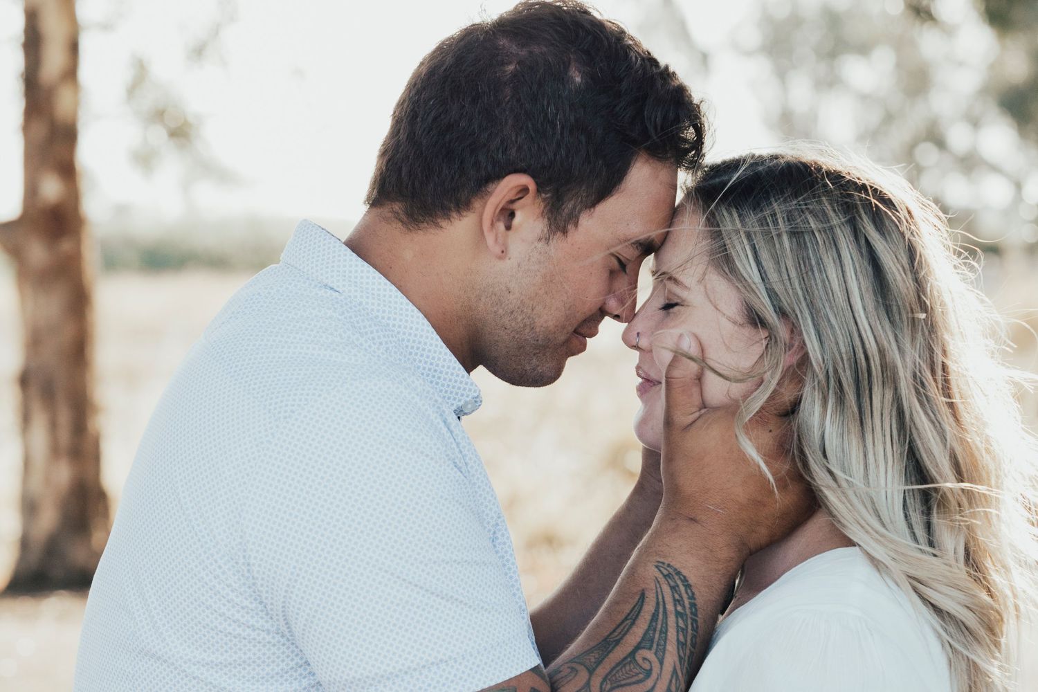 Intimate couple sharing tender moment outdoors with foreheads touching in soft natural lighting.