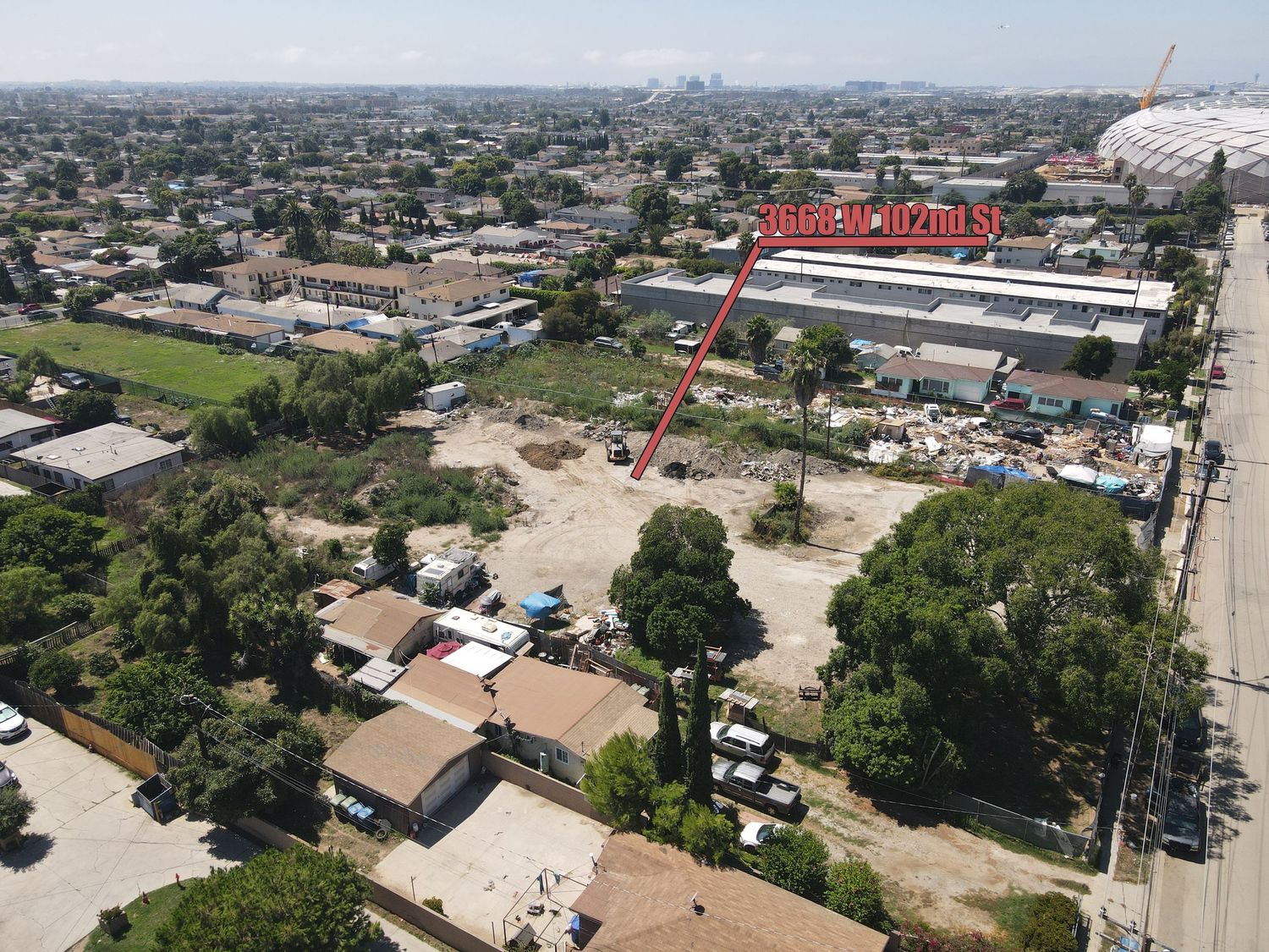 Aerial view of urban vacant lot near large stadium with surrounding residential and commercial buildings.