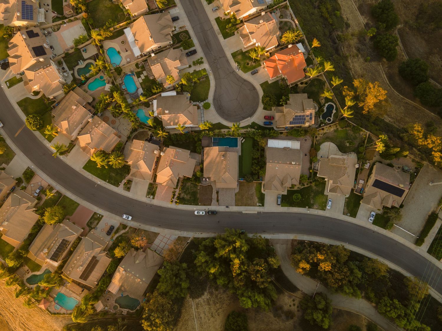 Aerial view of a suburban neighborhood with winding roads, swimming pools, and tree-lined streets at golden hour.