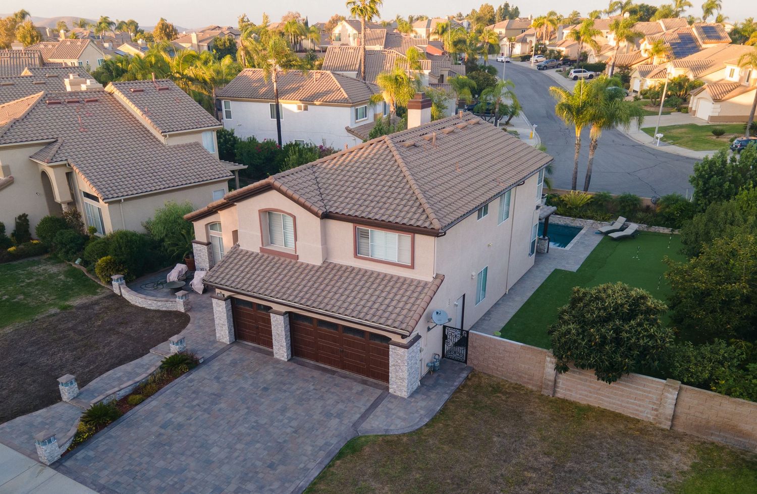 Aerial view of two-story Mediterranean home with tile roof, stone accents, and palm tree-lined street.