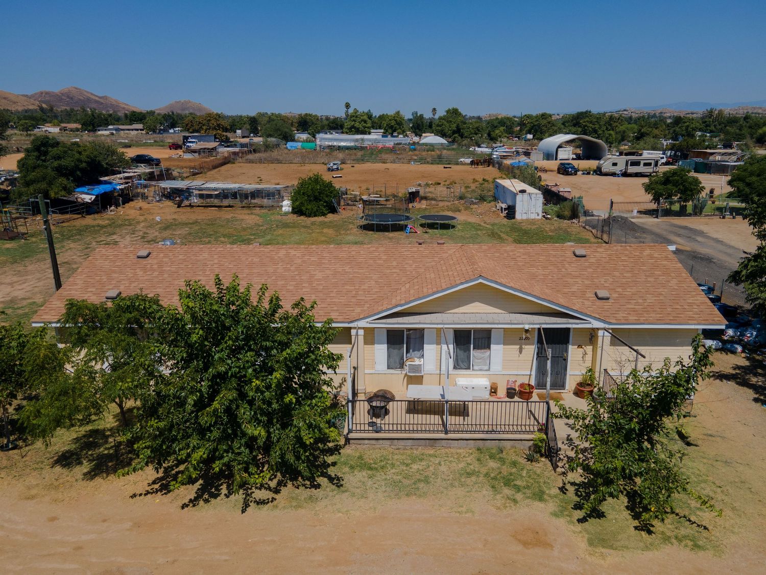 Aerial view of single-story home with covered porch, mature trees, and expansive rural property views.