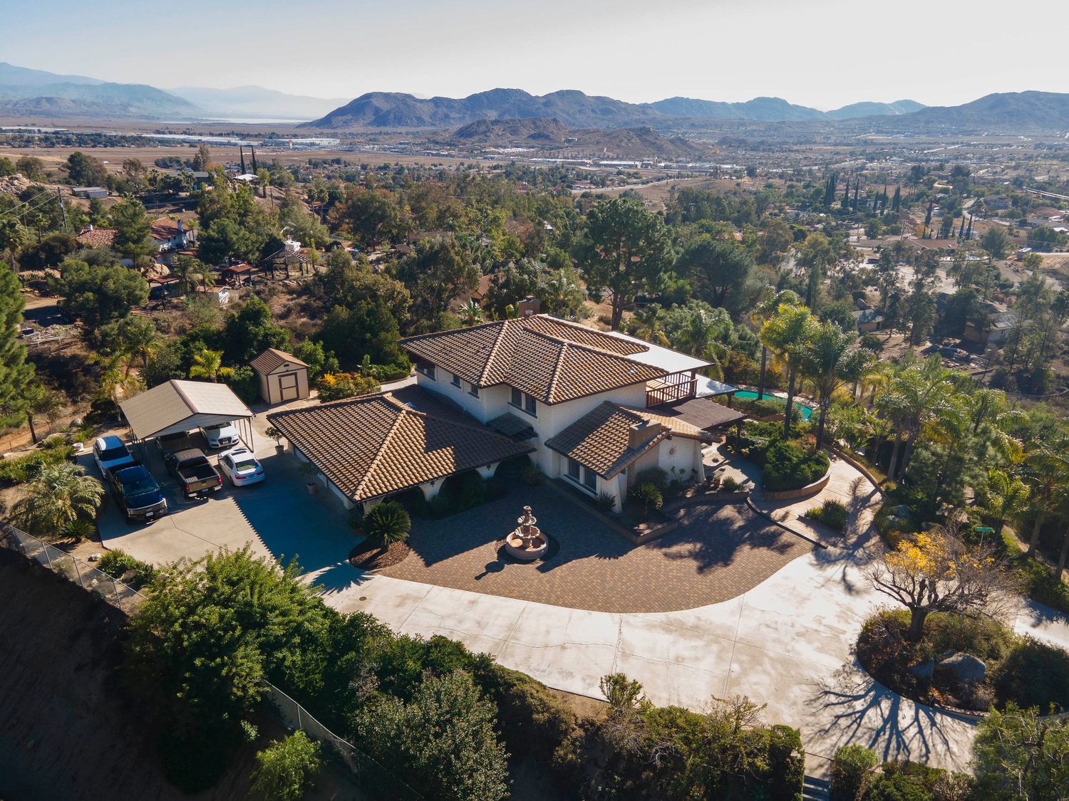Aerial view of a spacious hilltop home with a tile roof, large driveway, pool, and sweeping valley and mountain views.