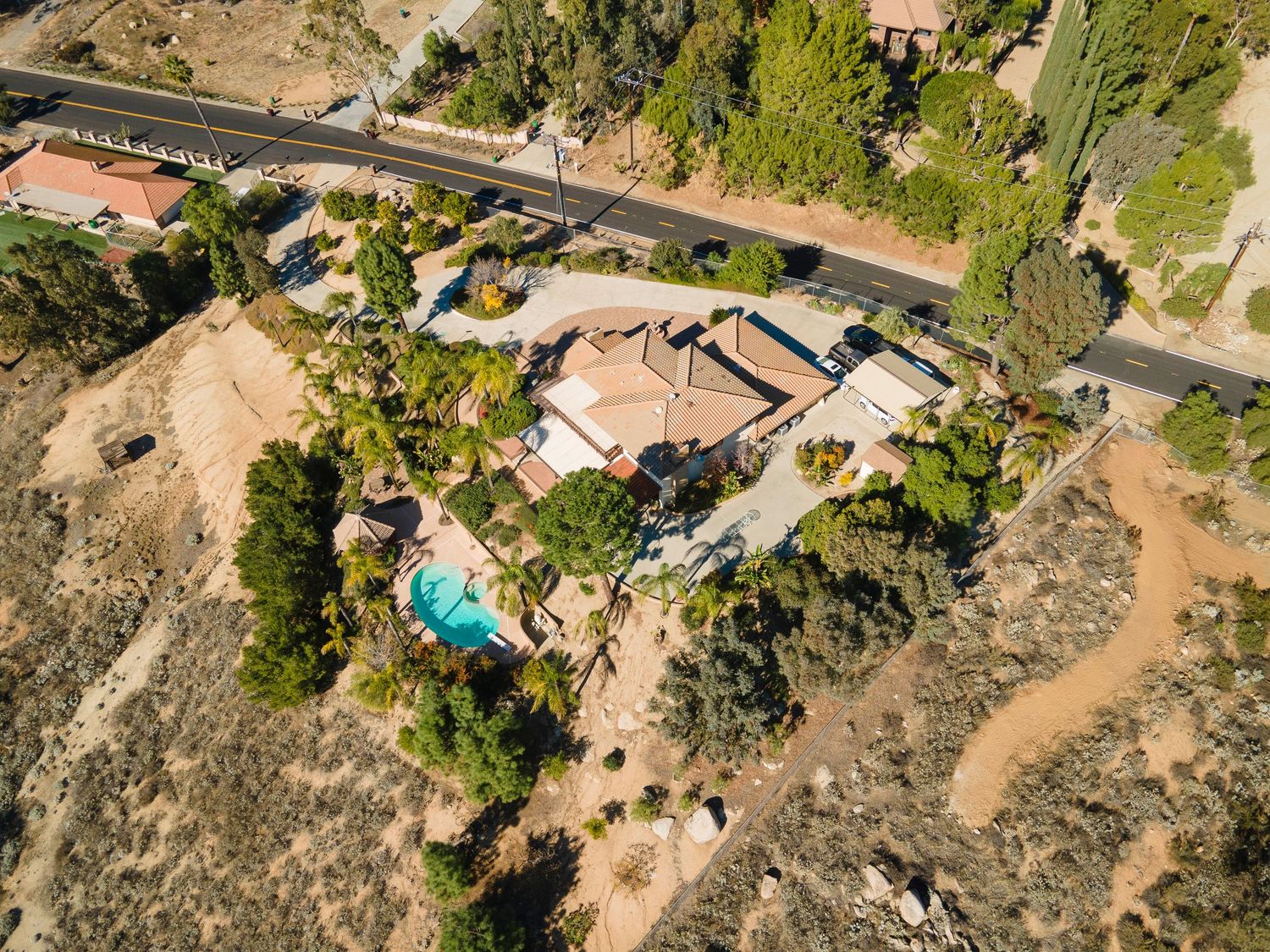Aerial view of a desert property featuring a pool, sparse vegetation, and a compact home in a dry California landscape.