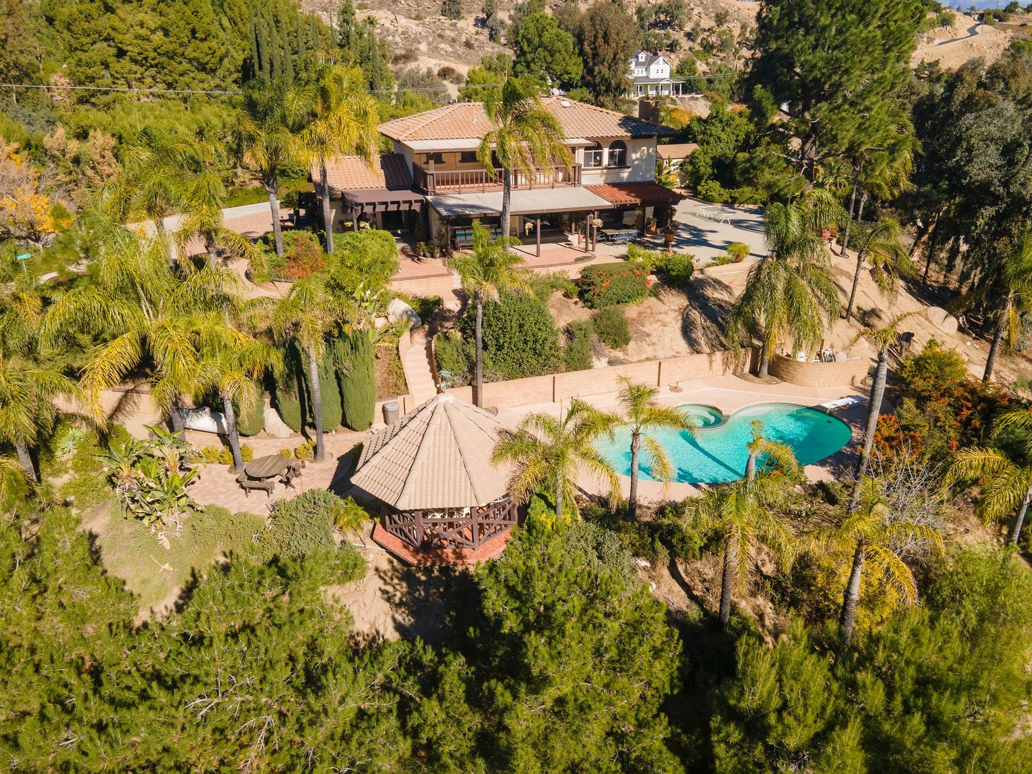 Aerial view of a hilltop estate with a pool, palm trees, and lush landscaping in a Southern California canyon.