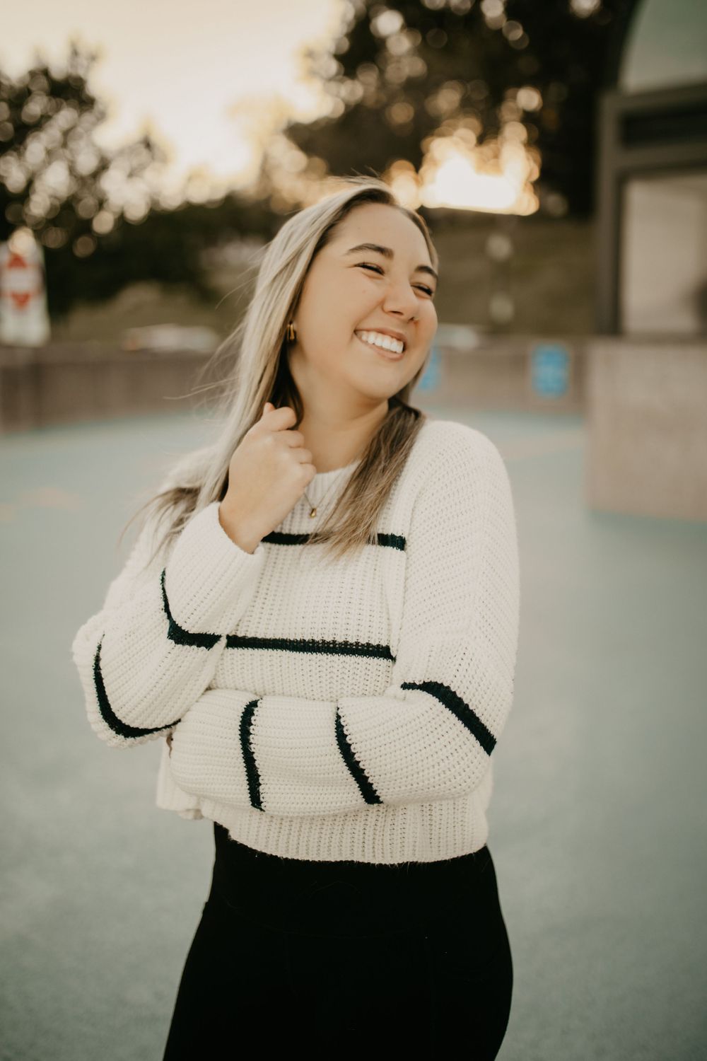 Joyful outdoor fashion portrait showcasing a cozy white striped sweater against sunset lighting.
