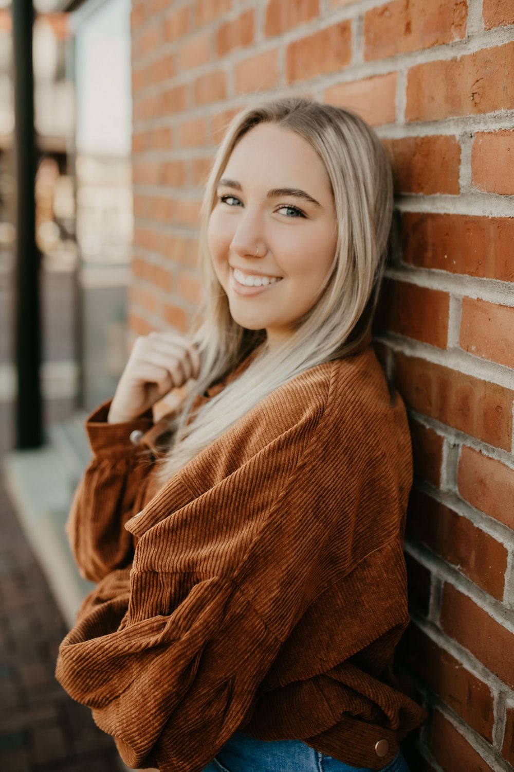 A portrait of someone in a brown corduroy jacket leaning against a brick wall.