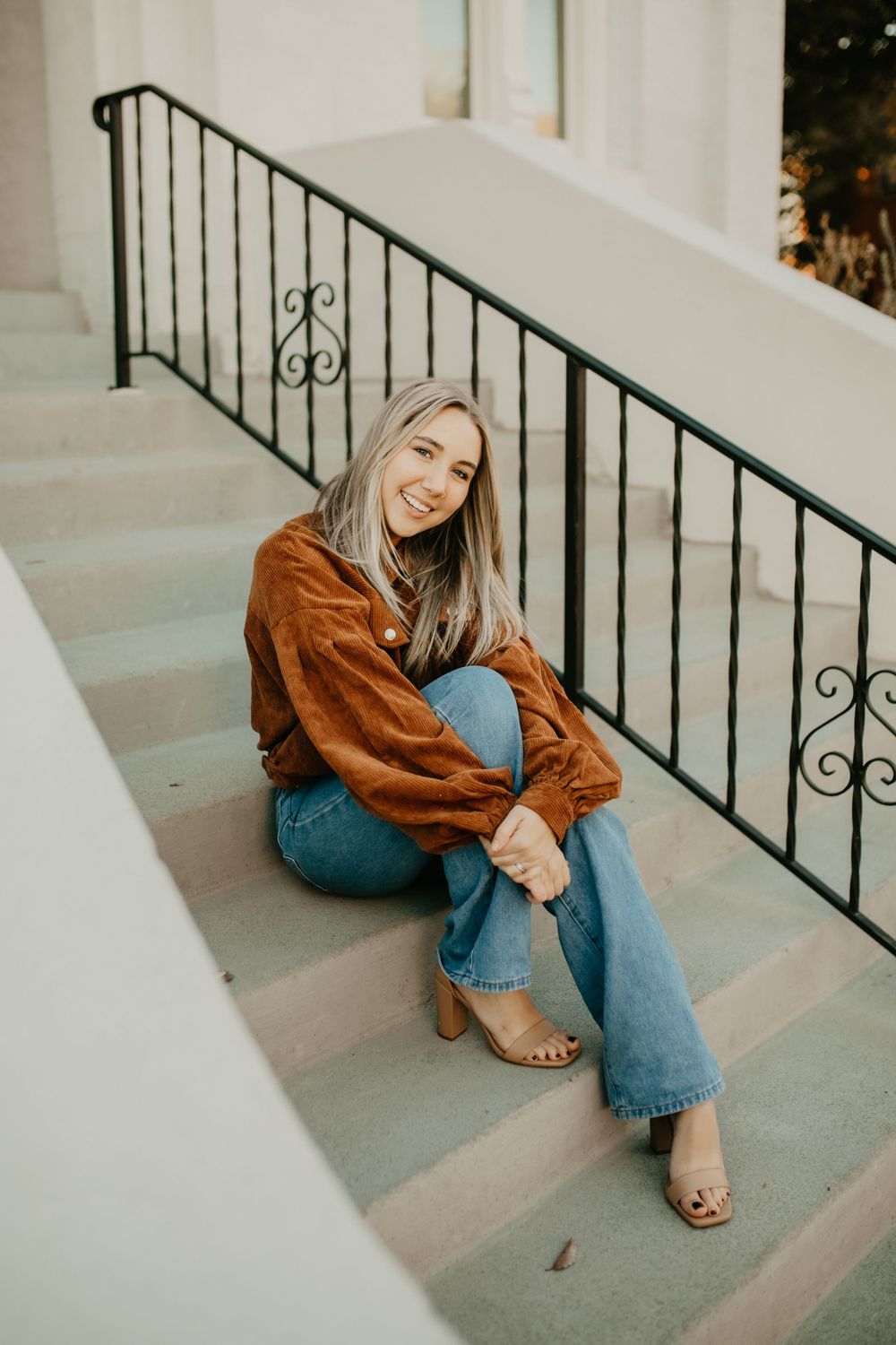 A casual portrait on white steps with decorative railings wearing denim and brown corduroy.