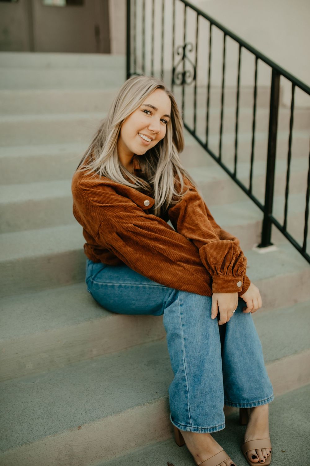 A casual lifestyle portrait showing a warm brown corduroy jacket paired with flared jeans on concrete steps.