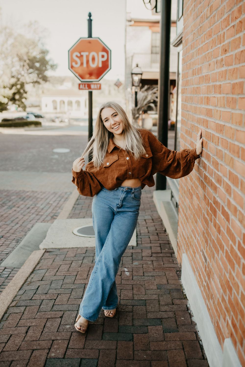 A casual street portrait next to a brick wall and stop sign wearing denim and brown corduroy.