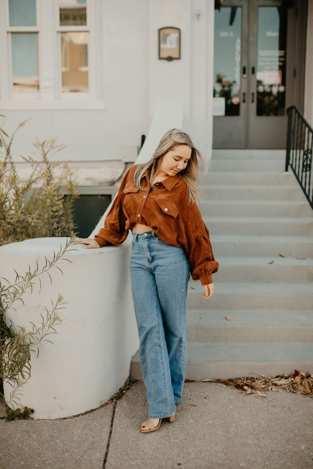Stylish autumn fashion shot featuring a brown corduroy jacket and flared jeans against white architecture.