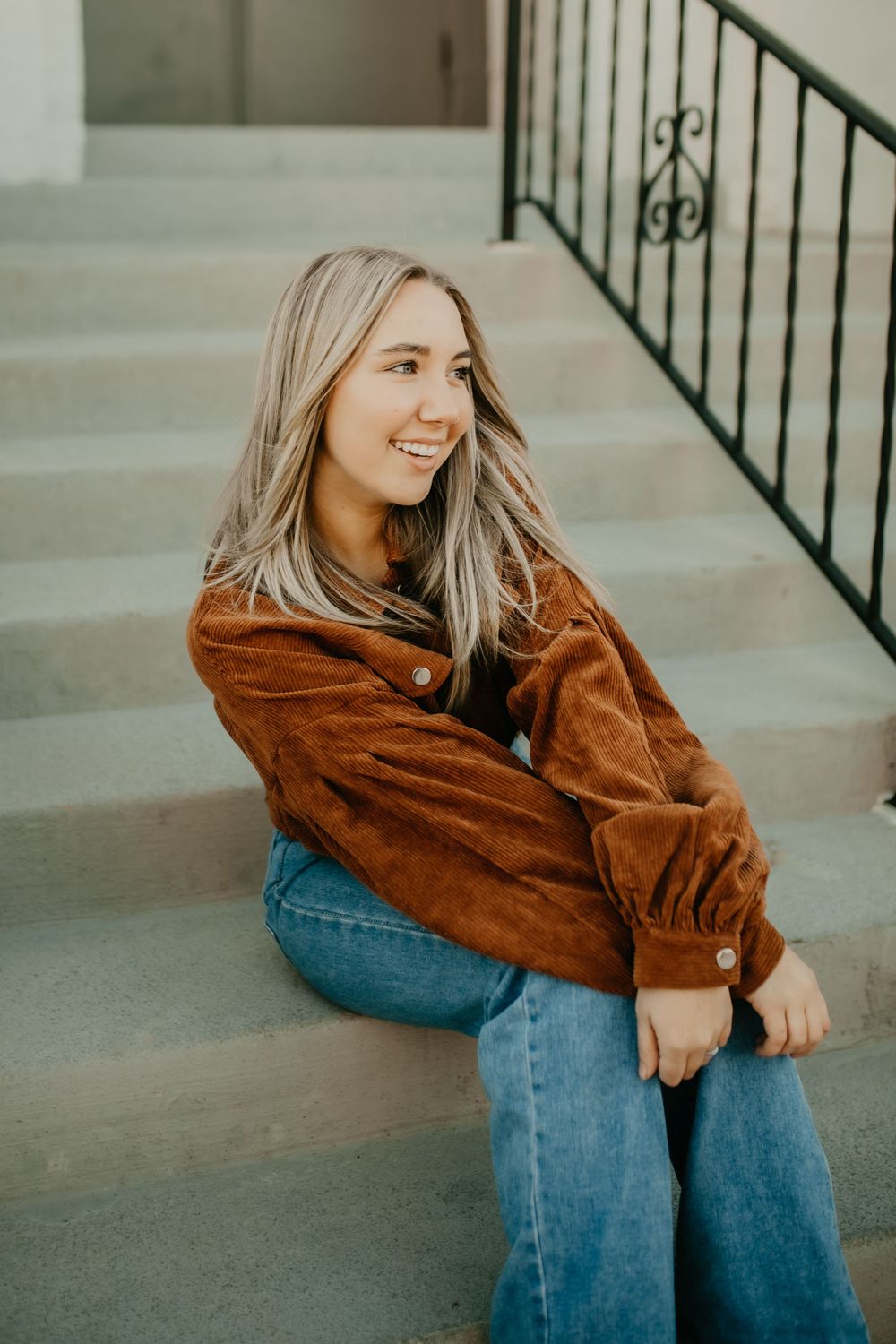 A relaxed portrait sitting on concrete steps with black metal railing wearing casual attire.