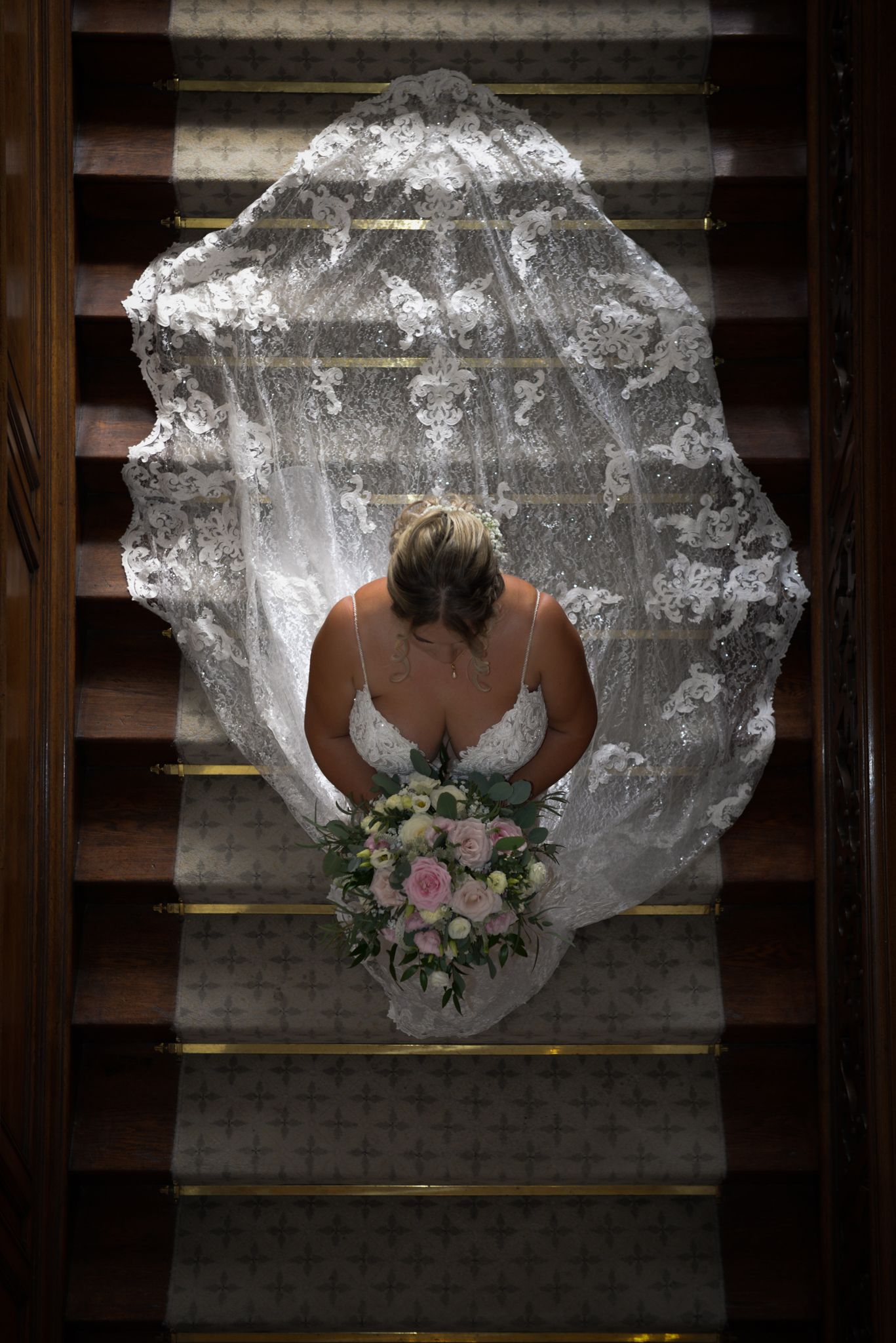 Overhead view of a flowing white wedding dress and bouquet on wooden stairs.