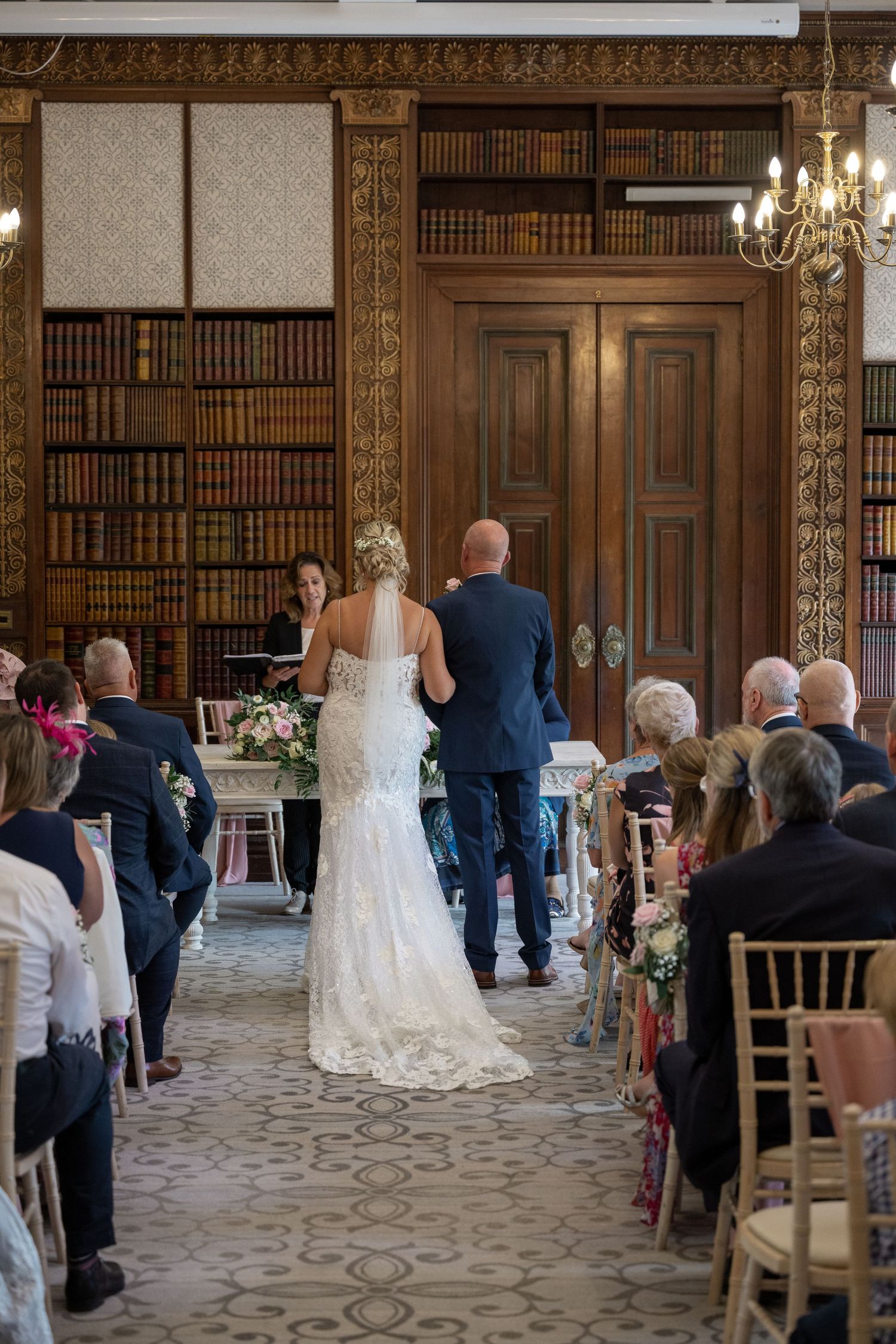Wedding ceremony in an elegant library with wooden paneling and bookshelves.