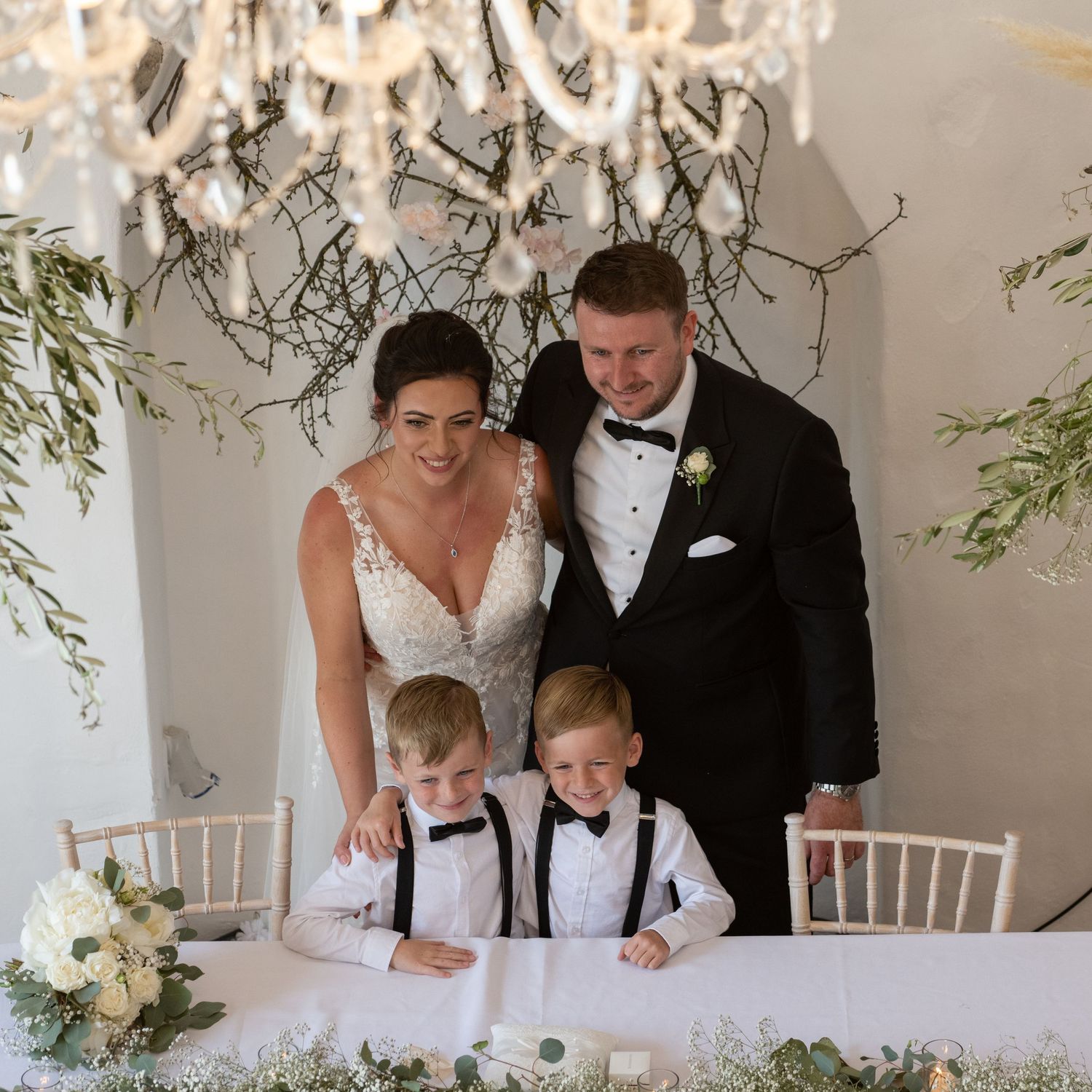 A formal family wedding portrait with decorative branches and white floral arrangements.