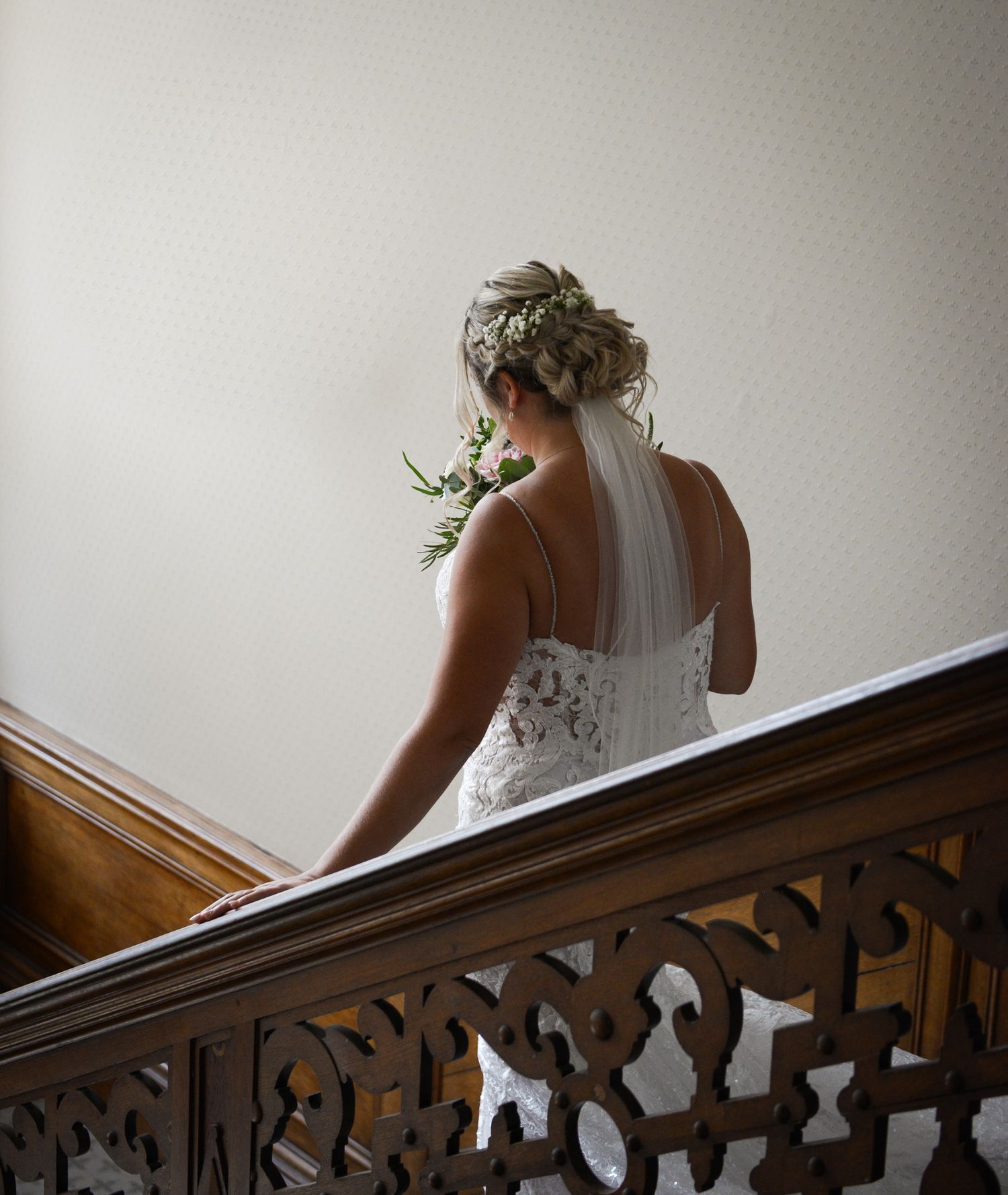 Back view of a wedding dress with delicate lace details against wooden staircase railing.