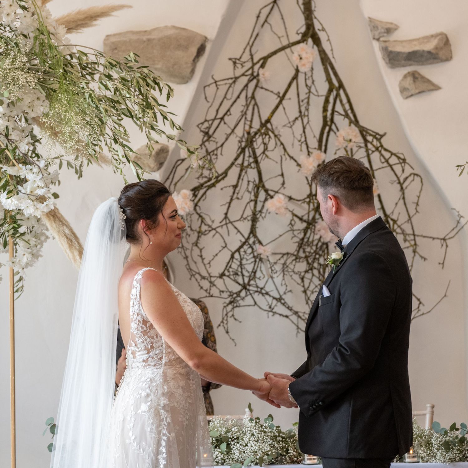 A wedding ceremony moment under an arch decorated with rustic branches and greenery.