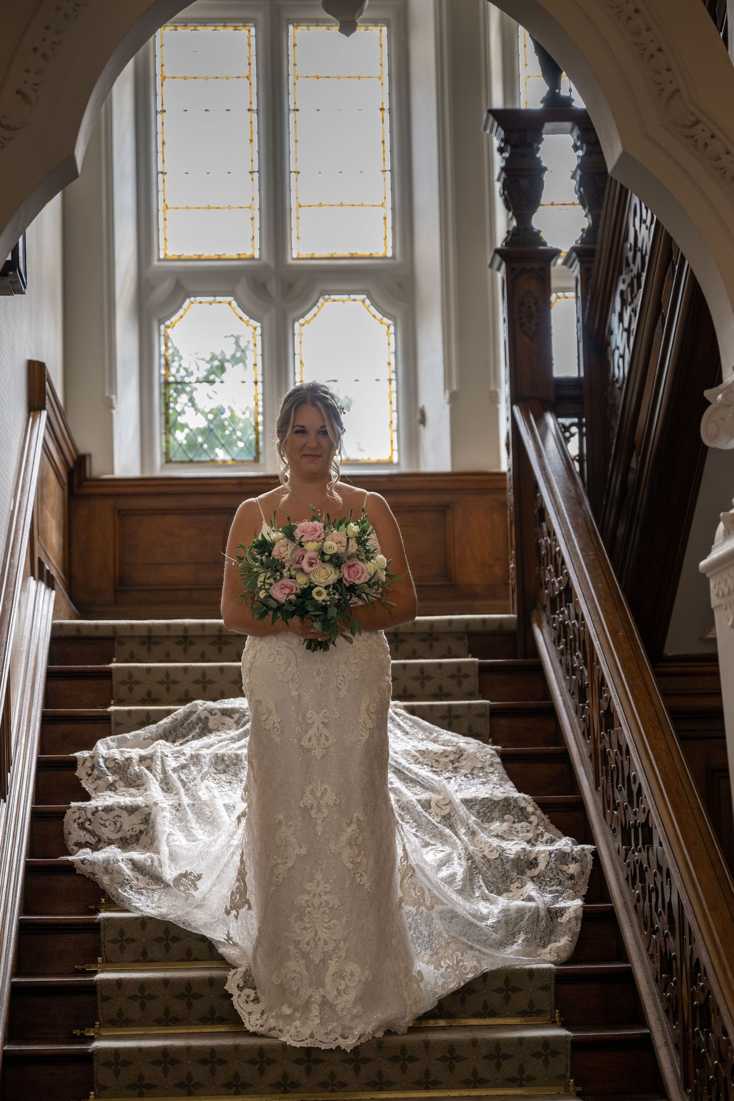 Beautiful wedding dress with trailing lace train photographed on an elegant wooden staircase.