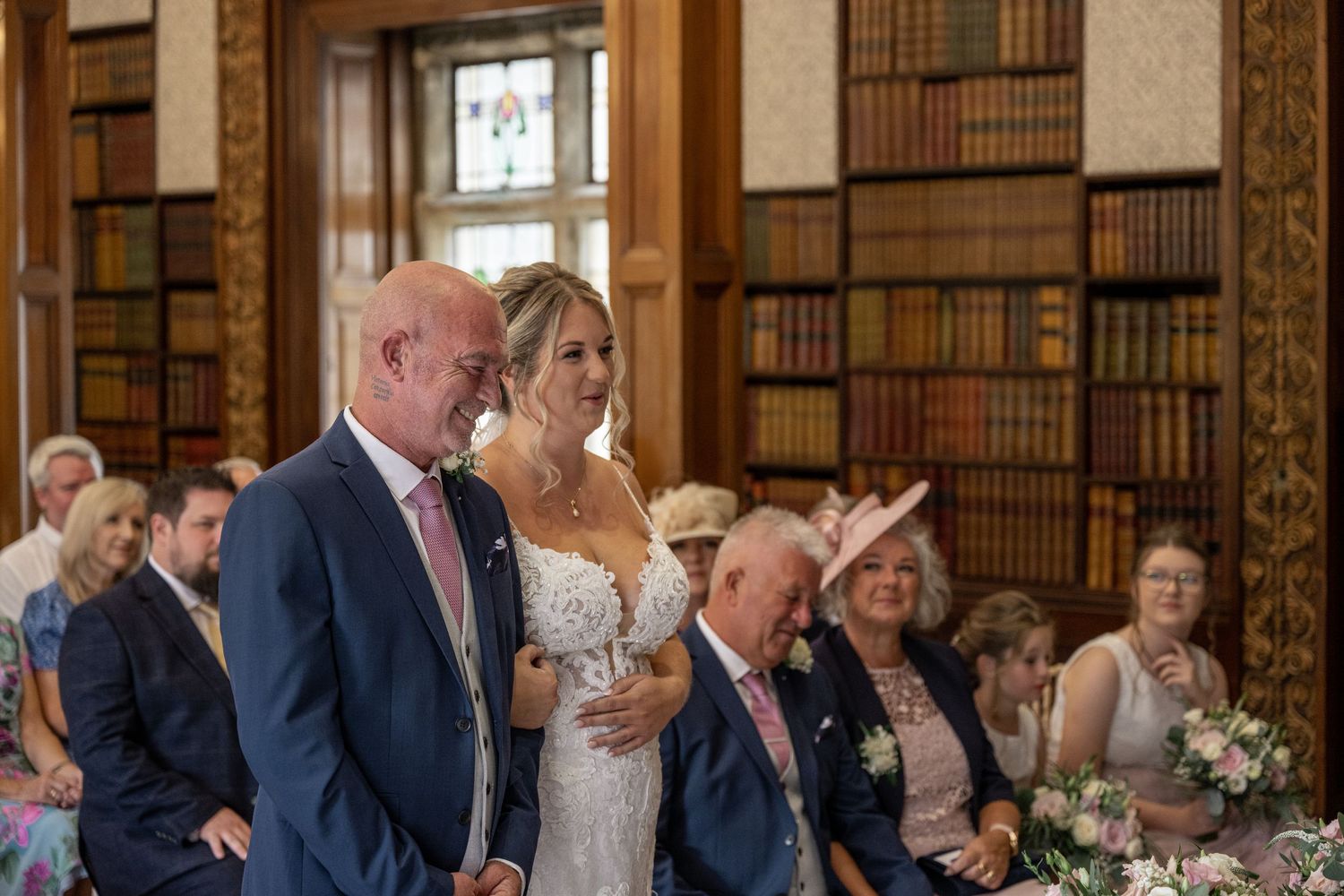 Wedding ceremony taking place in an elegant library with ornate bookshelves and chandelier lighting.