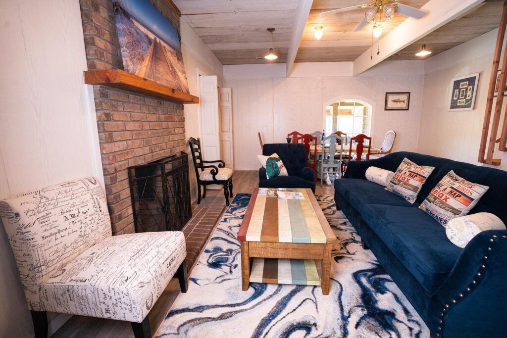 Cozy living room with brick fireplace, blue sofa, patterned rug, and rustic coffee table in warm lighting.