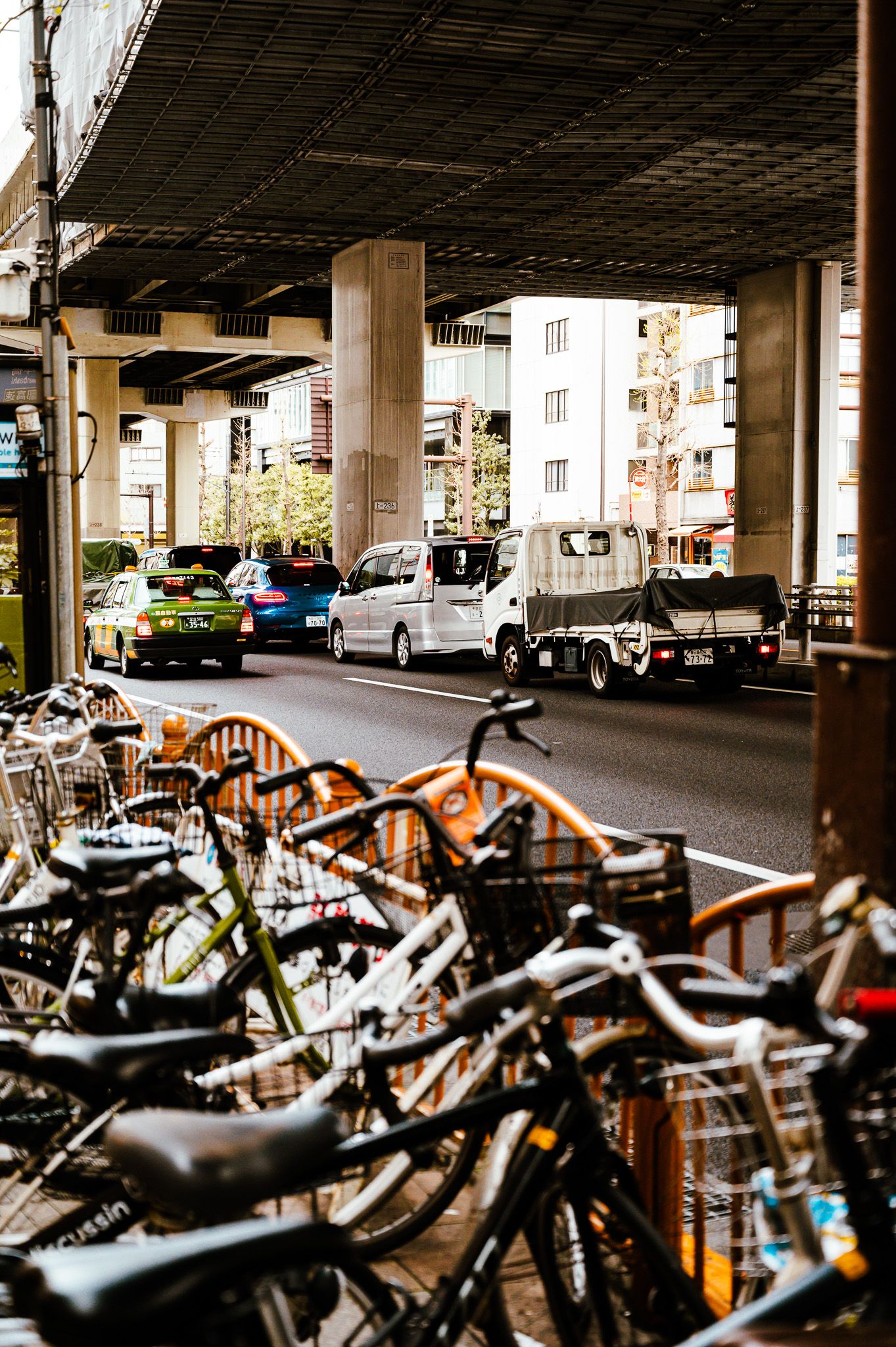 Row of parked bicycles beneath an elevated highway with cars and buildings in the background.