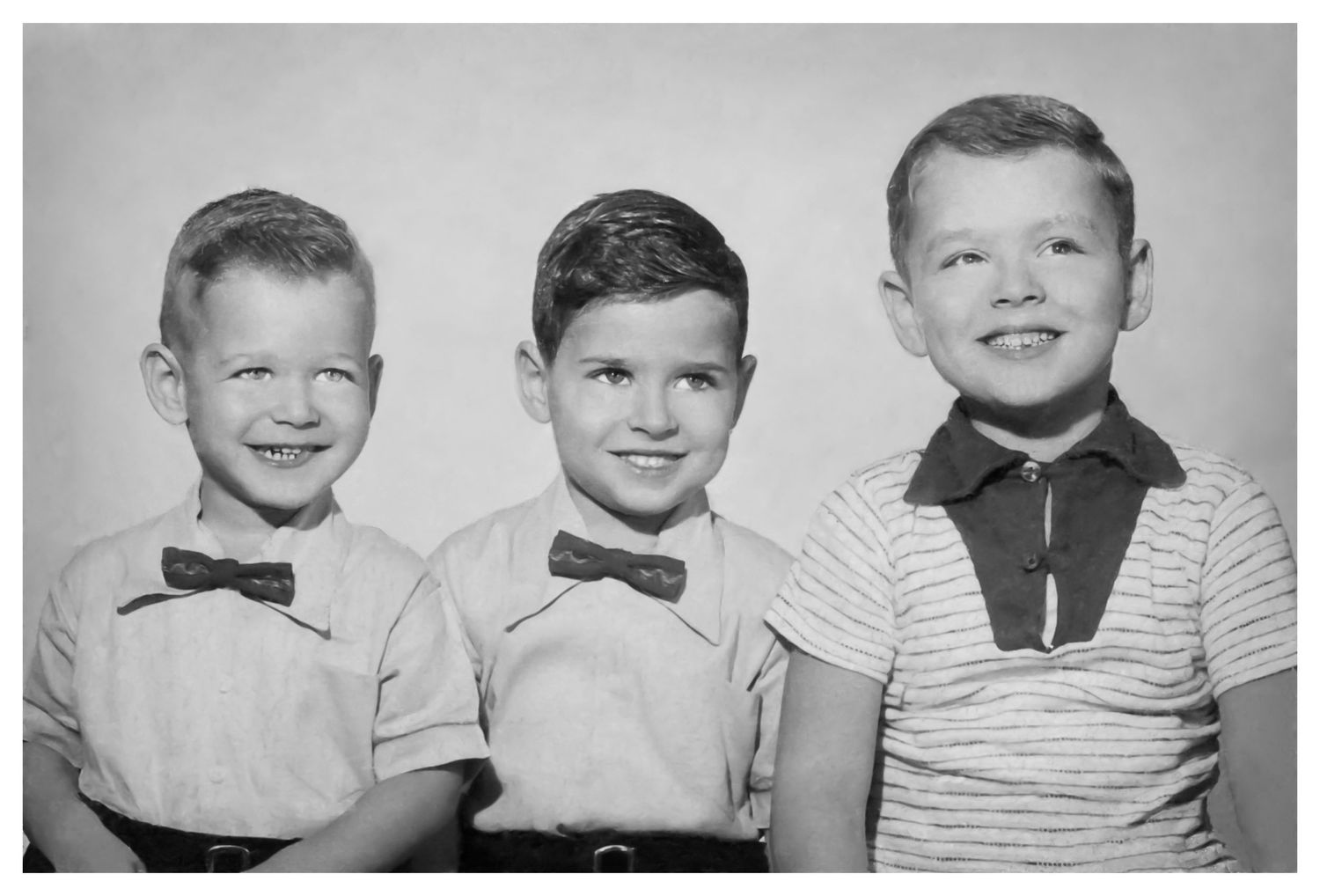 Black and white studio photograph of three boys in matching outfits from a bygone era.