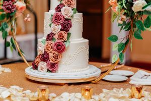 Wedding cake decorated with dusty rose flowers and greenery on a wooden table with candlelight.