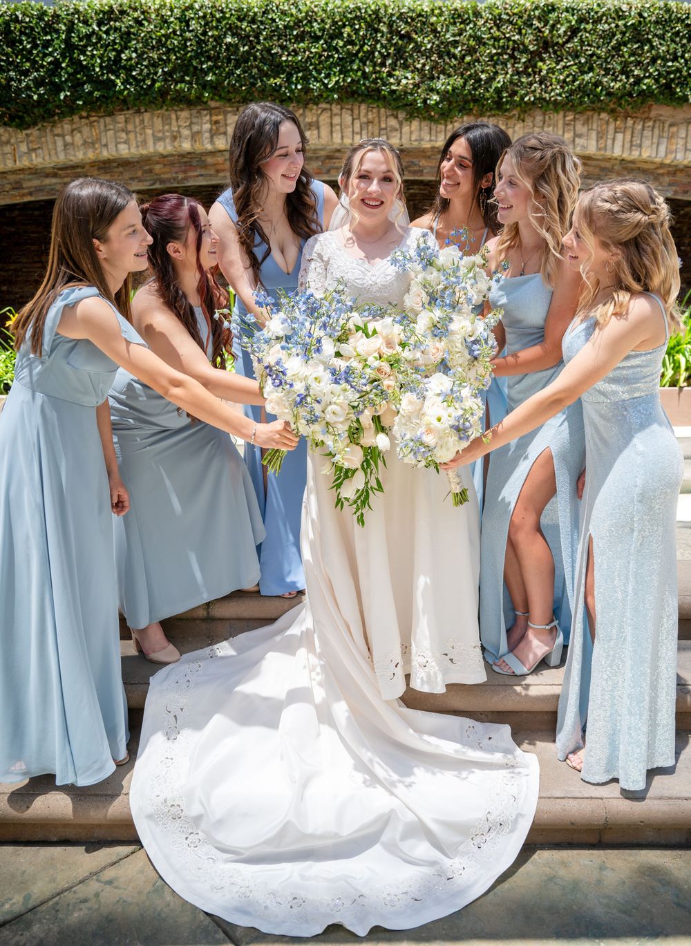 Bride and bridesmaids in light blue dresses share a joyful moment while holding floral bouquets.