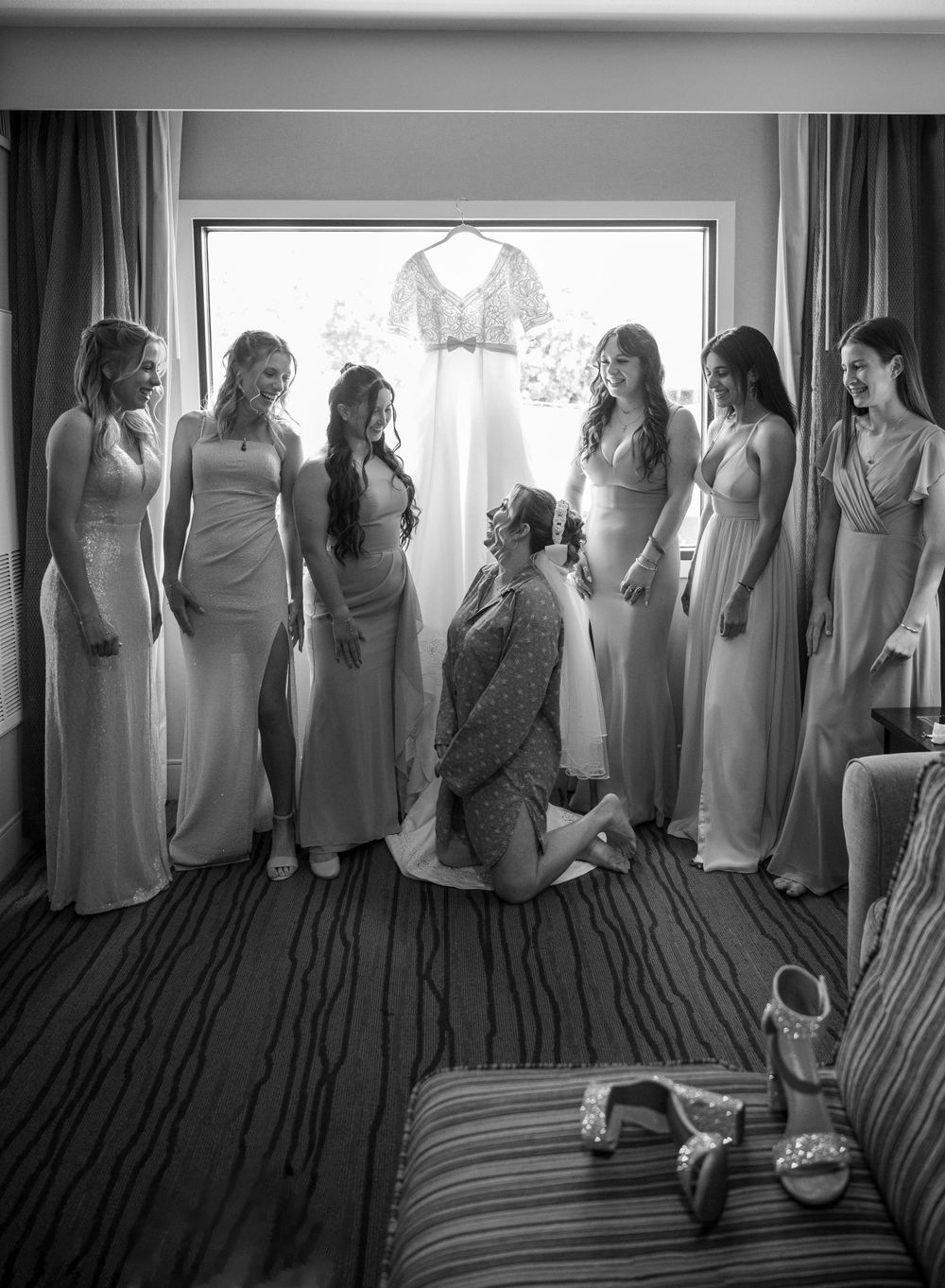 Wedding party poses together in a hotel room with bridal gown displayed in window.