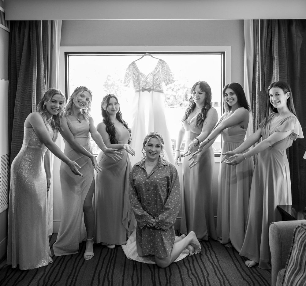 Bridesmaids in matching dresses gather around a central figure in a joyful getting-ready moment.