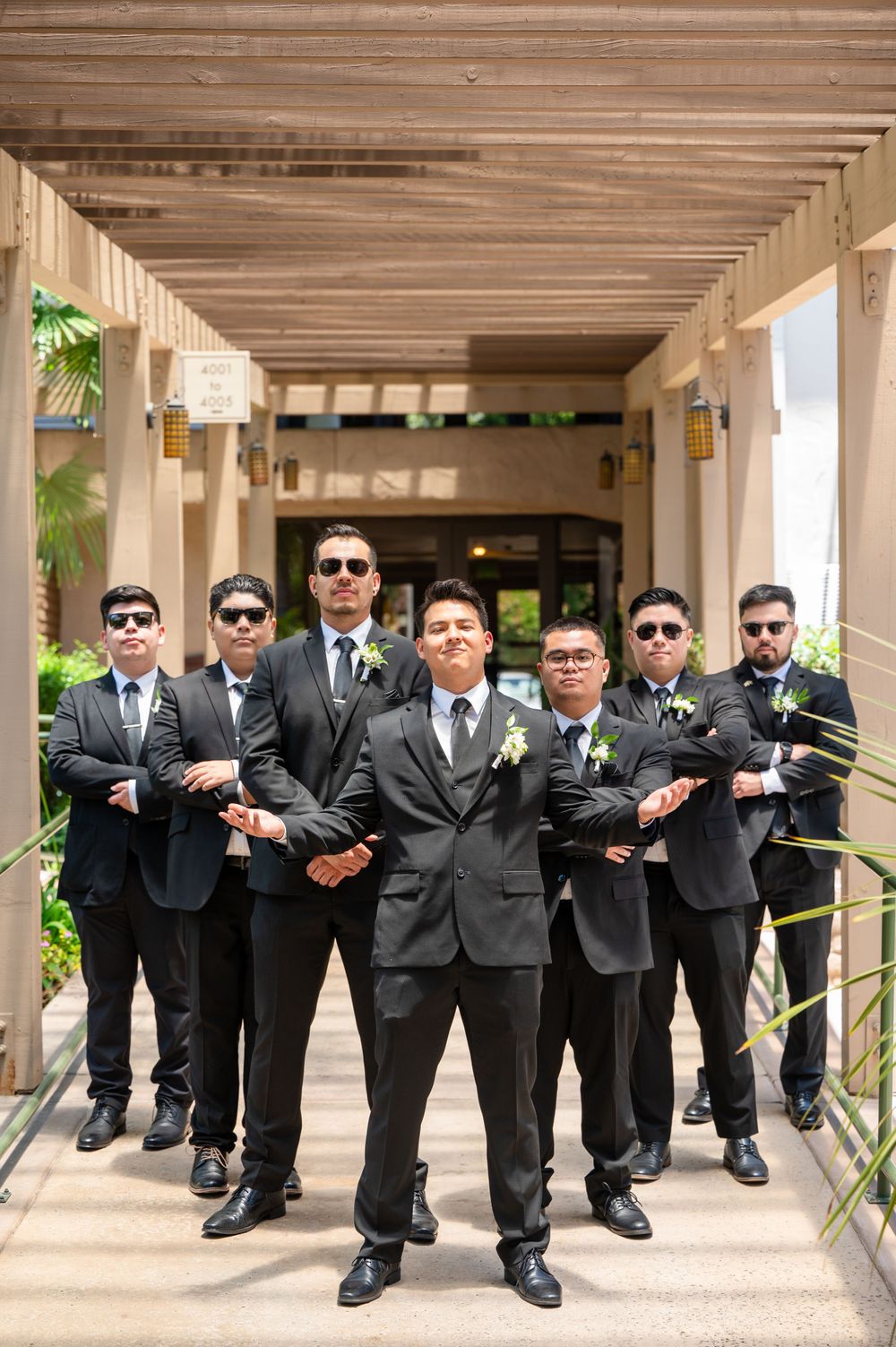 Groomsmen in dark suits and sunglasses pose dramatically in outdoor corridor.