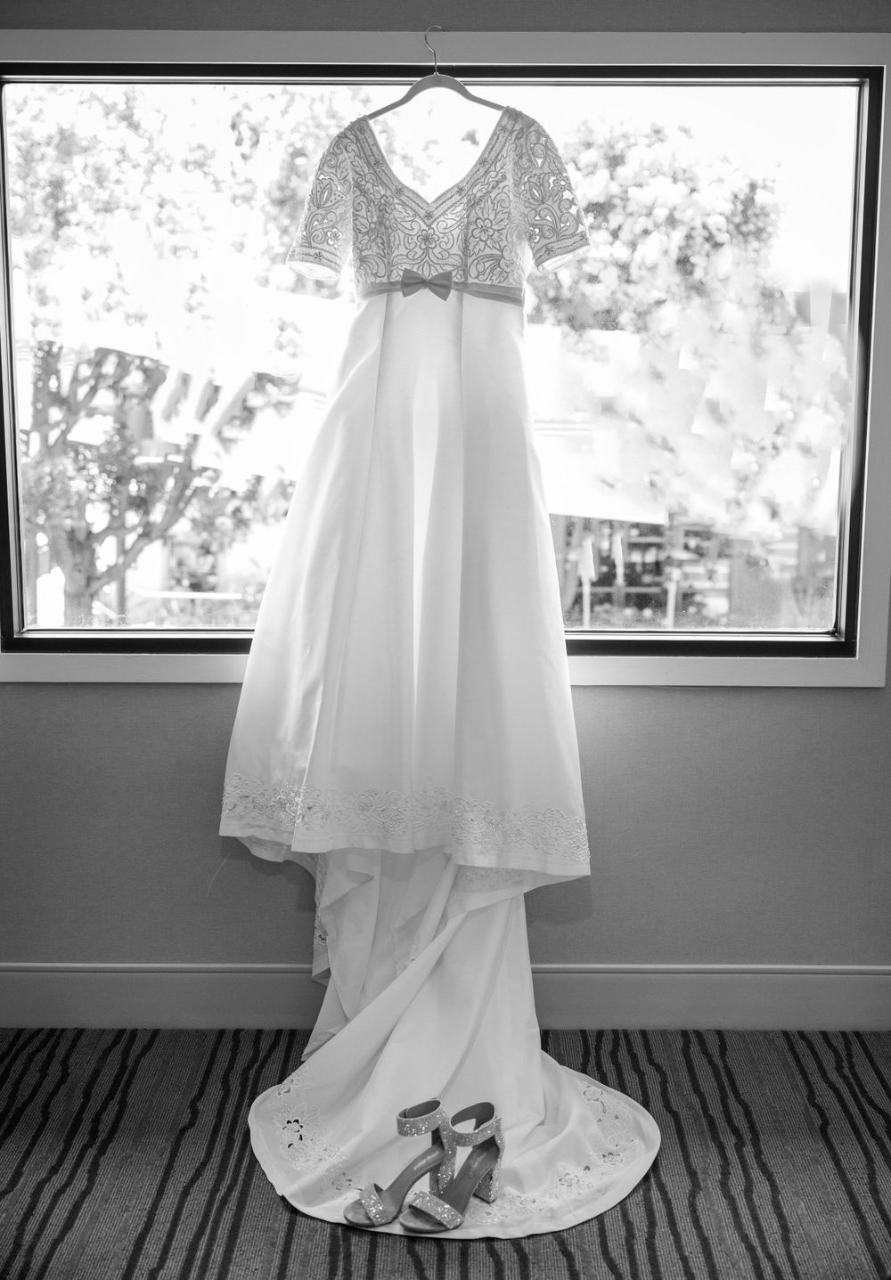 Elegant white wedding gown with lace bodice hanging in window display showing long train and detailed embellishments.