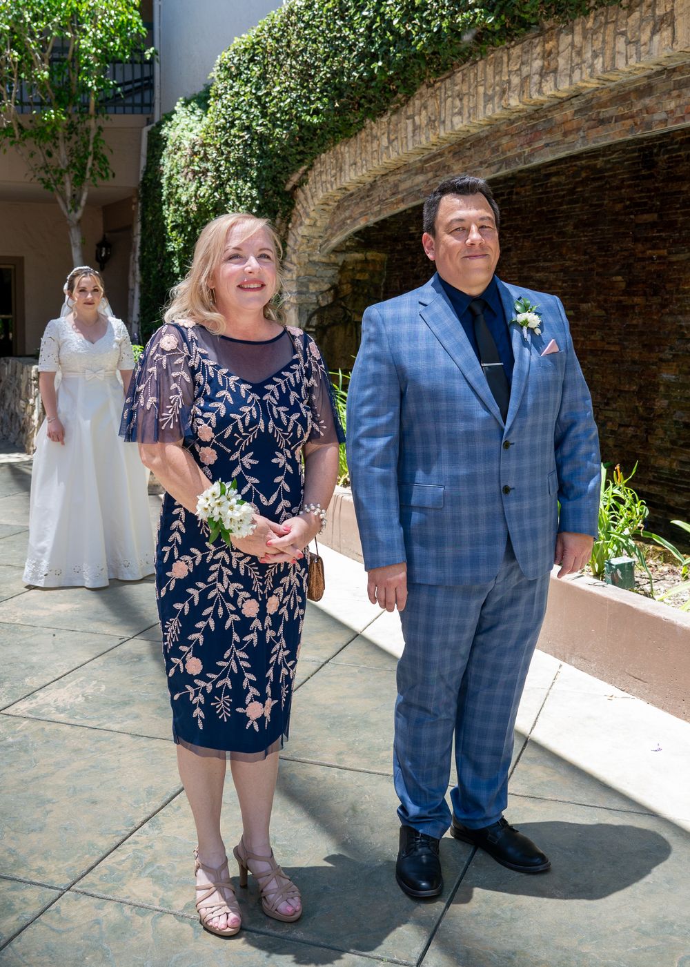 Wedding guests in formal attire stand on decorated outdoor patio.
