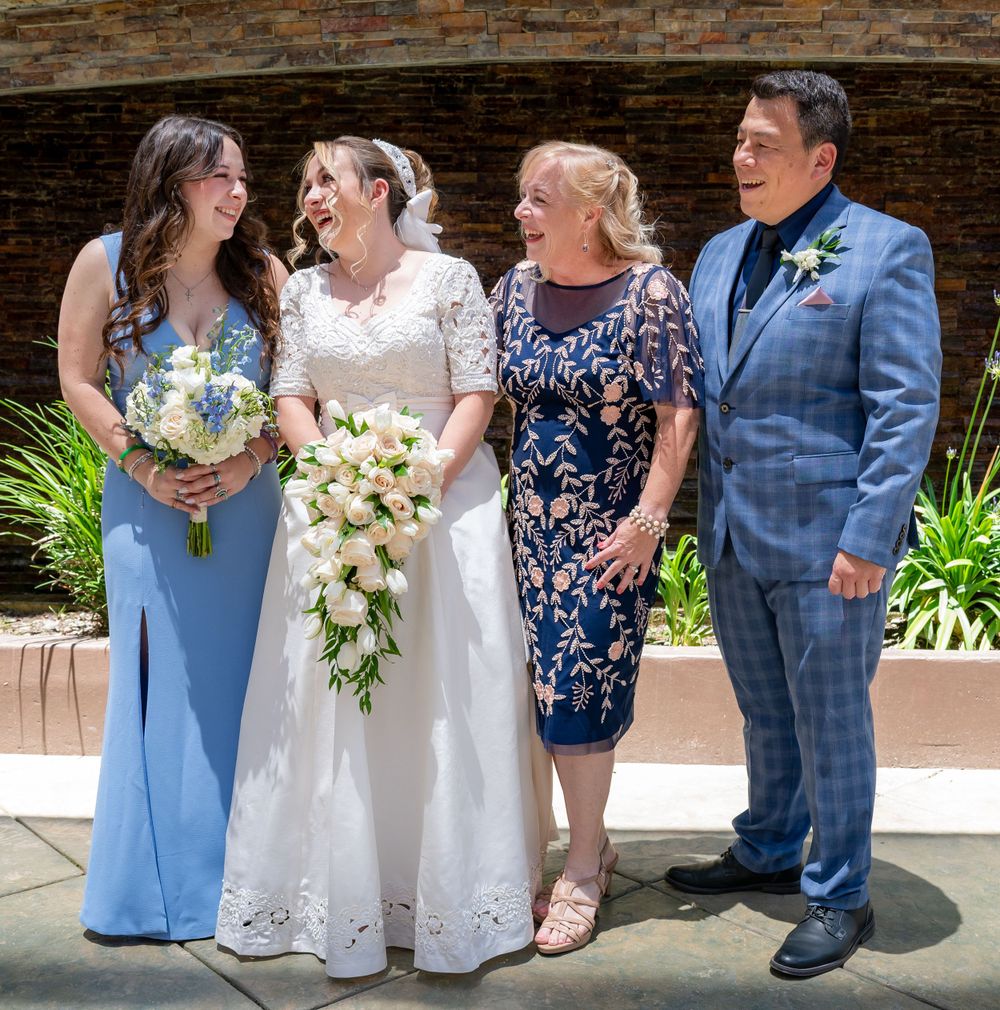 Wedding party in blue attire and formal dress pose together under a brick archway with floral bouquets.