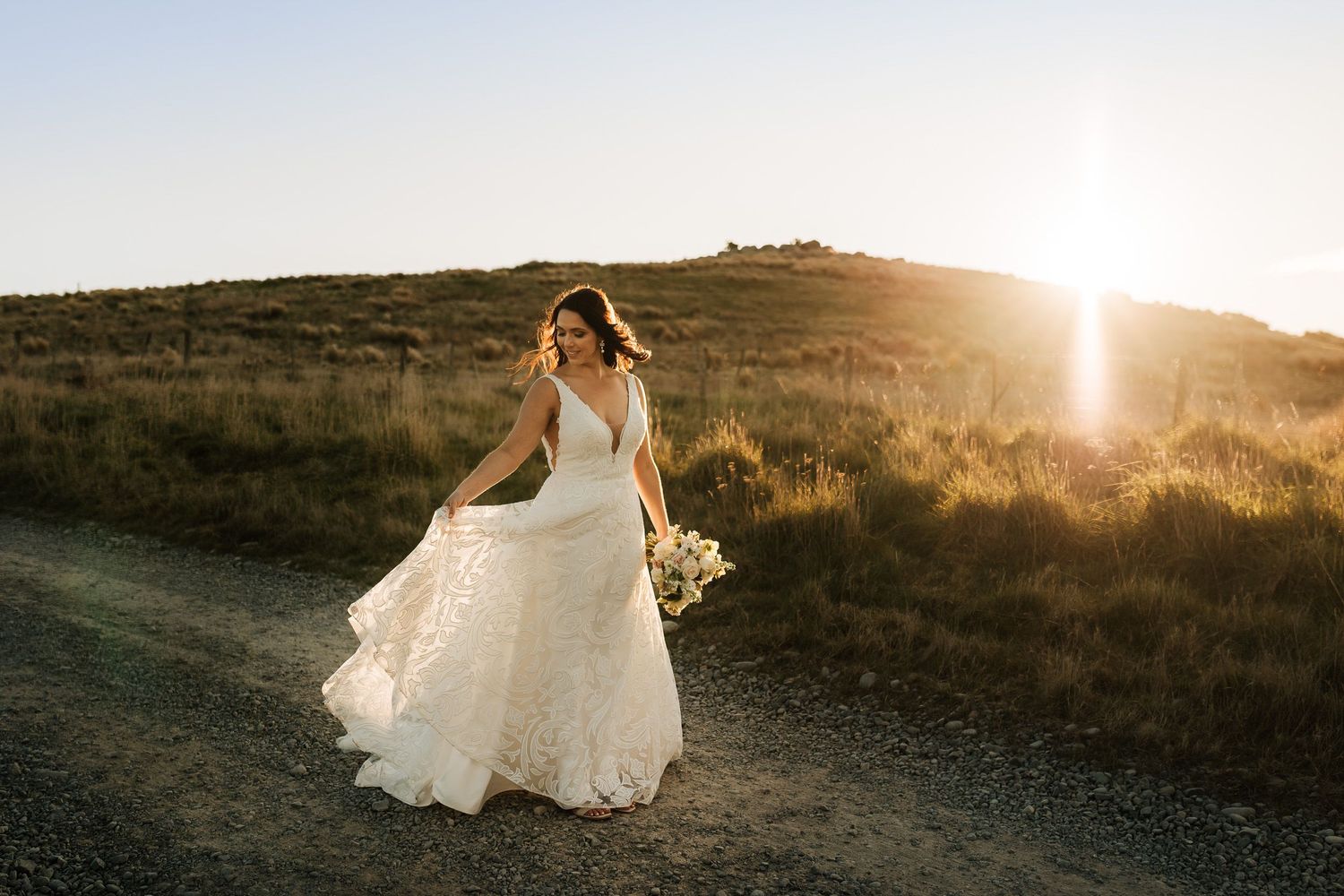Bride in flowing dress at sunset in Port Hills Christchurch, holding bouquet