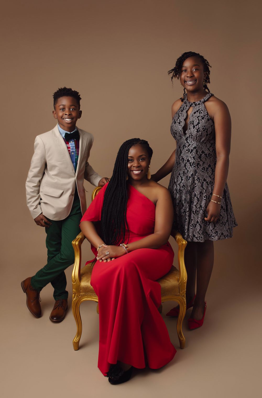 Family portrait session with formal attire featuring gold accent chair against brown backdrop.