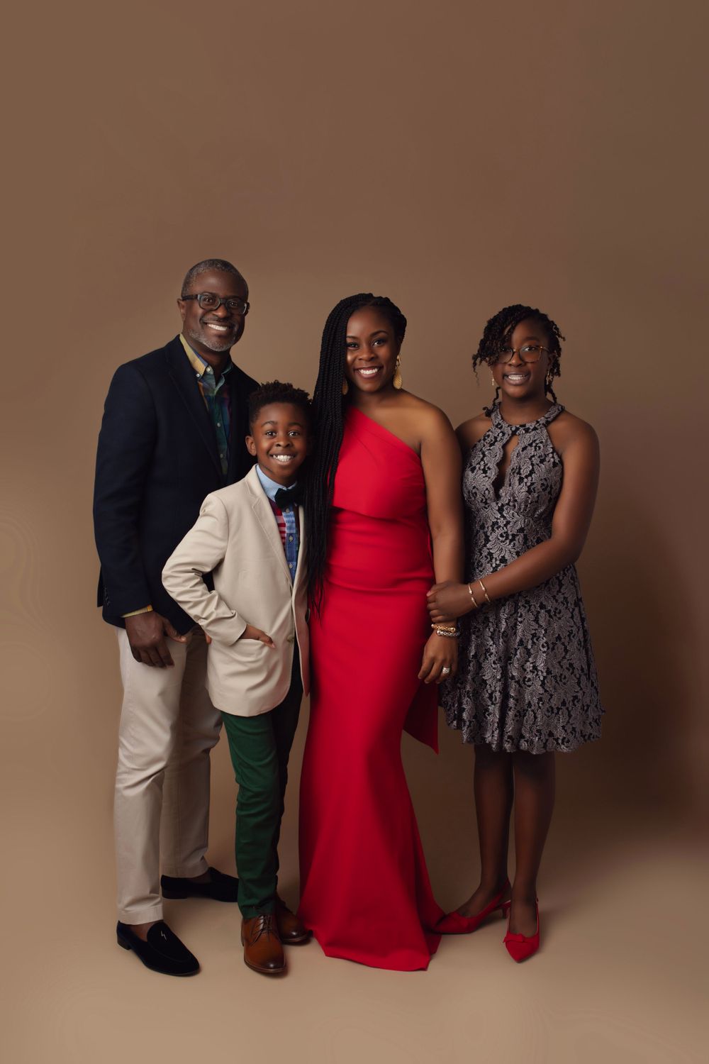 Family portrait session featuring coordinated formal wear with a red dress and suits against neutral background.