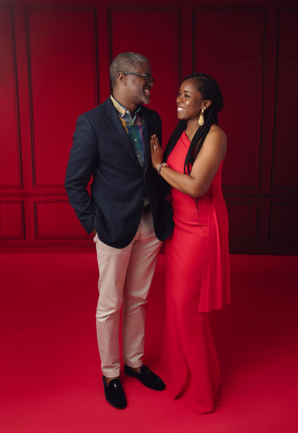 Elegant couple poses in formal attire against dramatic red backdrop in studio setting.